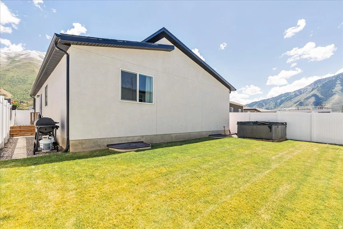Spacious backyard featuring a manicured lawn, white privacy fencing, and a built-in spa