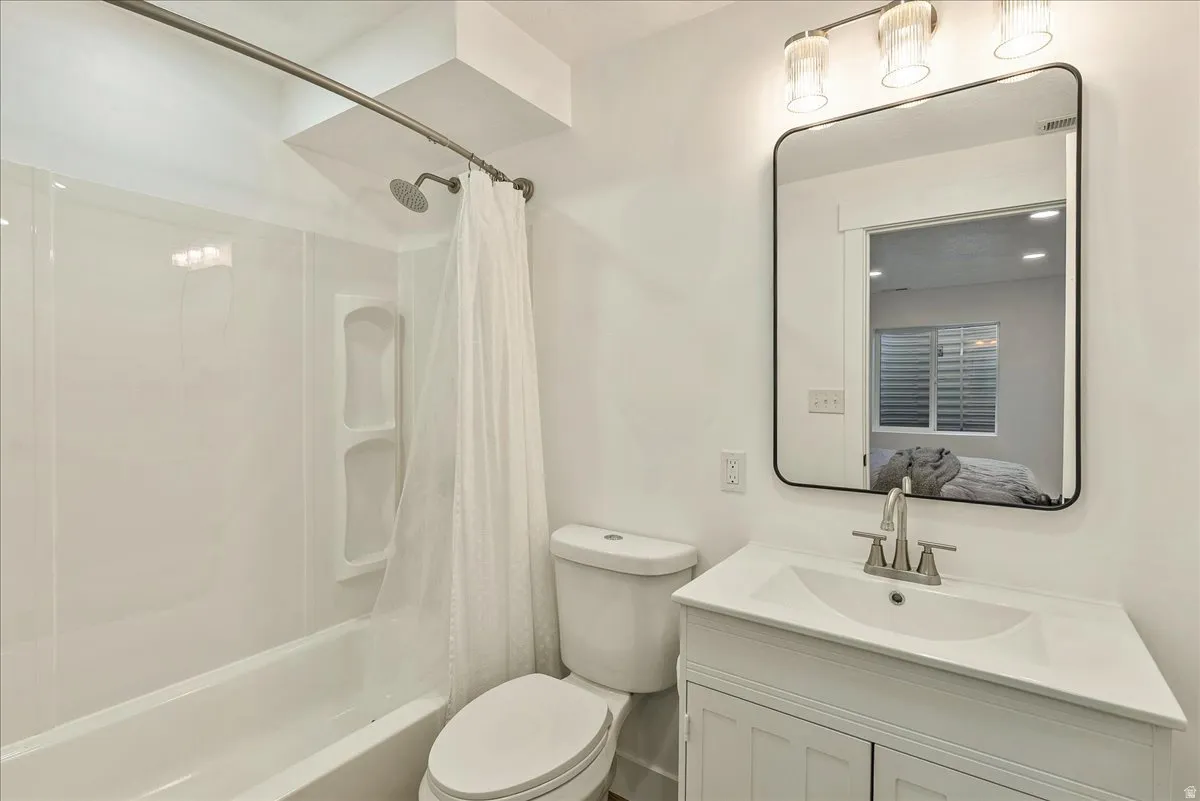 Bathroom featuring a white vanity with integrated sink, brushed nickel faucet, a rectangular framed mirror, and a full-size bathtub with an overhead shower and built-in shelving