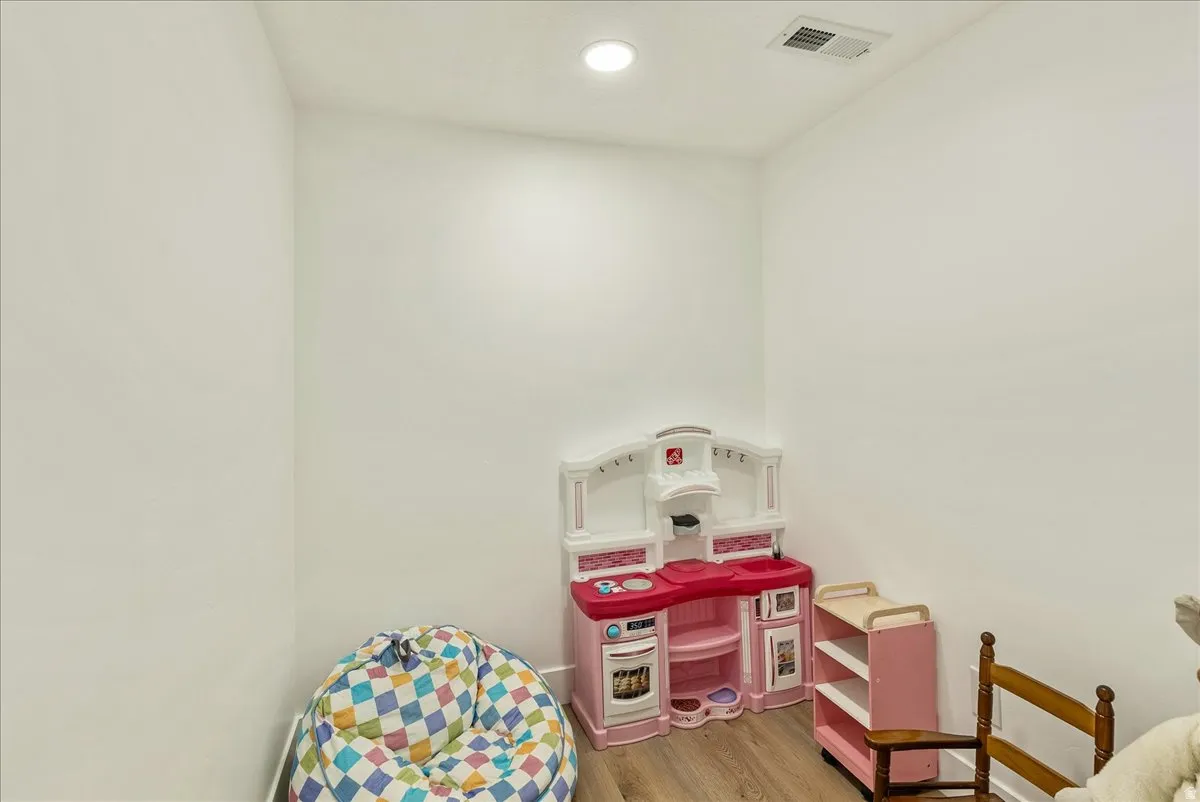Recessed ceiling lighting illuminates a room with light-toned walls and wood-finish flooring