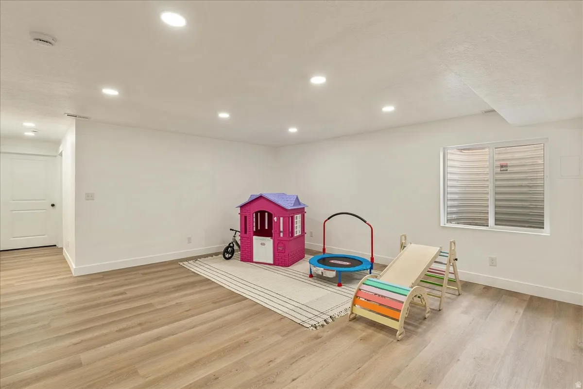 Spacious lower-level room featuring wood-finish flooring, recessed lighting, and bright white walls