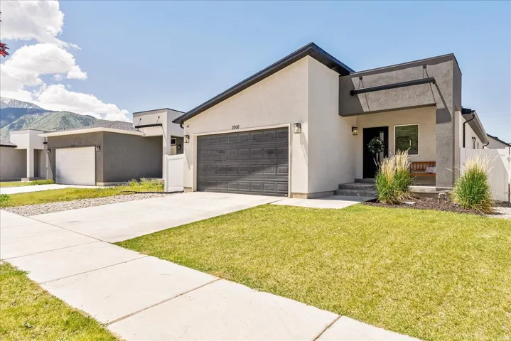 Contemporary stucco exterior featuring a dark gray garage door, a covered entry, and a manicured lawn