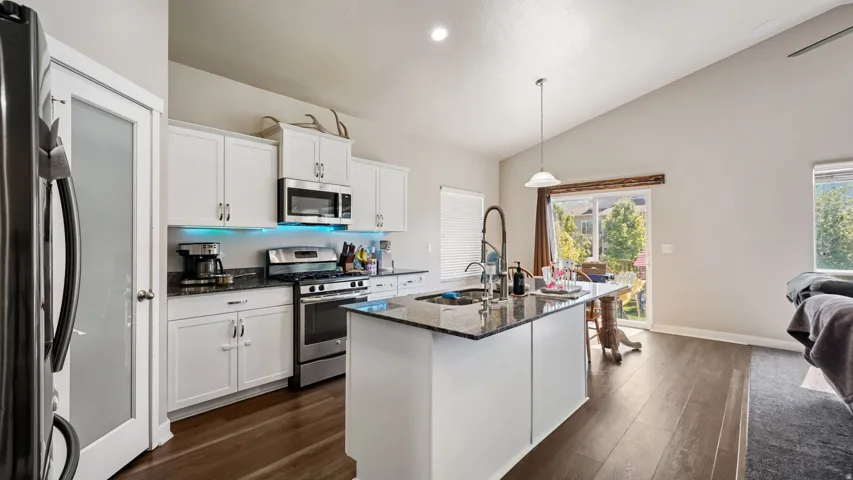 Open-concept kitchen featuring white cabinetry, stainless steel appliances, granite countertops, a center island with a sink, and LVP