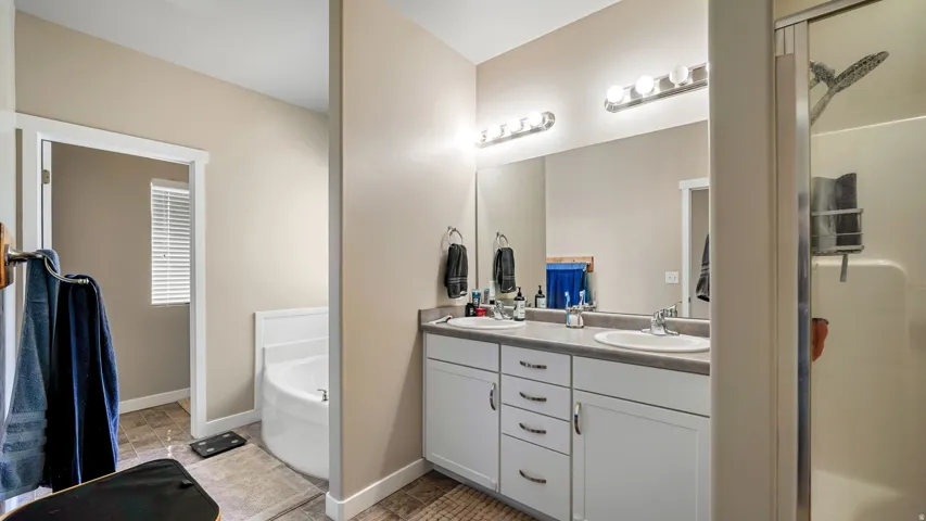 Primary Bathroom featuring a double vanity with white cabinetry and integrated sinks, a corner soaking tub, and a separate glass-enclosed shower