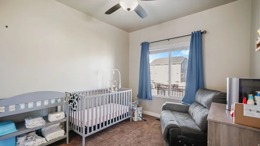 Upstairs Bedroom featuring neutral wall tones, a ceiling fan with light fixture, a window with blue curtains, and brown carpet flooring