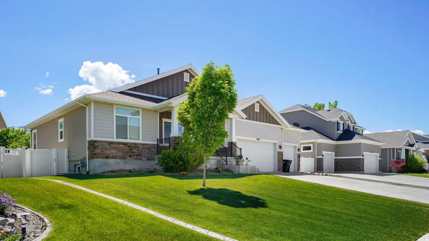Contemporary home featuring a stone and siding facade, a manicured front lawn, a white picket fence, a dedicated driveway, and an attached two-car garage
