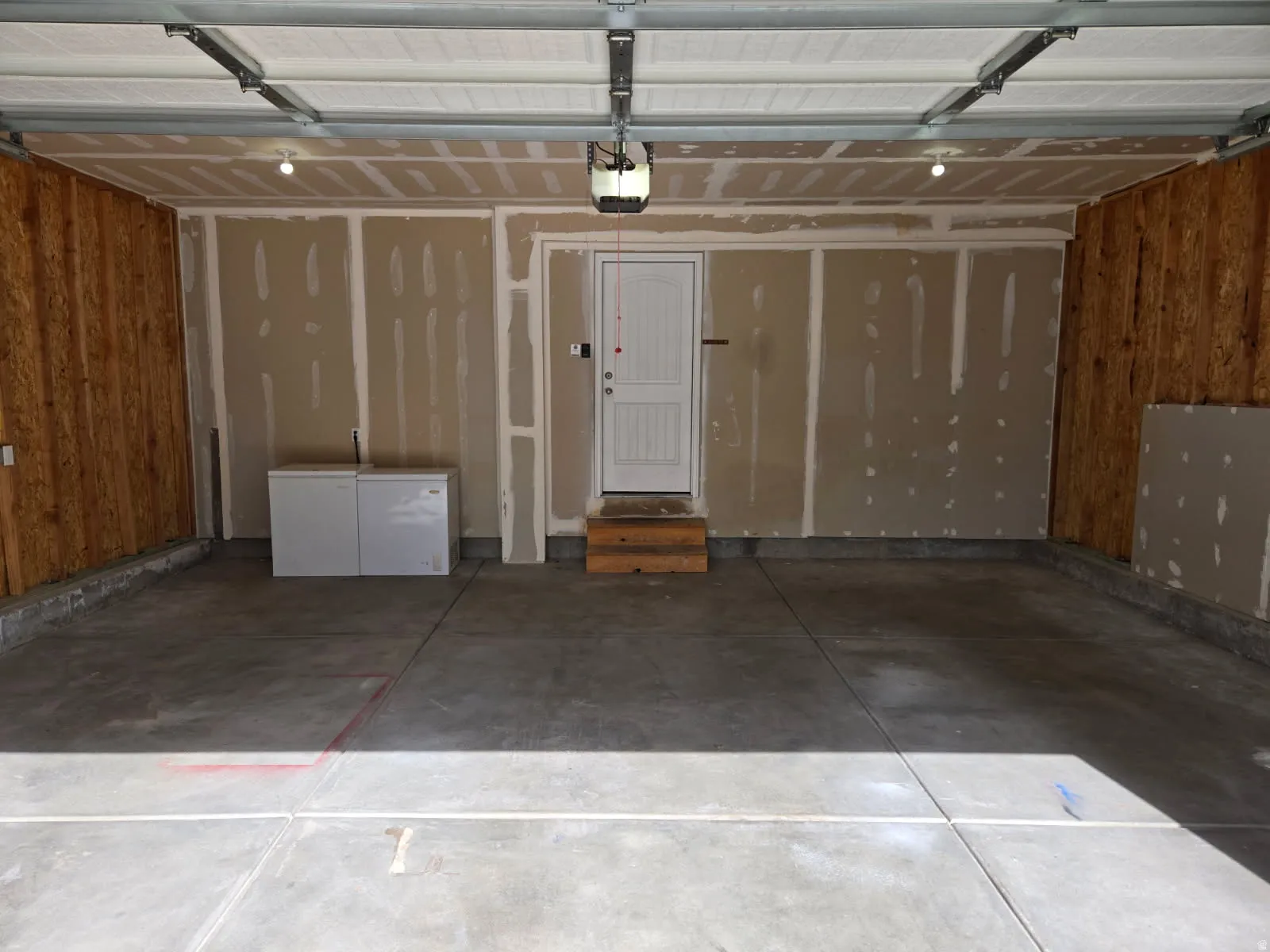 Spacious garage with concrete flooring, exposed wood-paneled walls, and a white interior door
