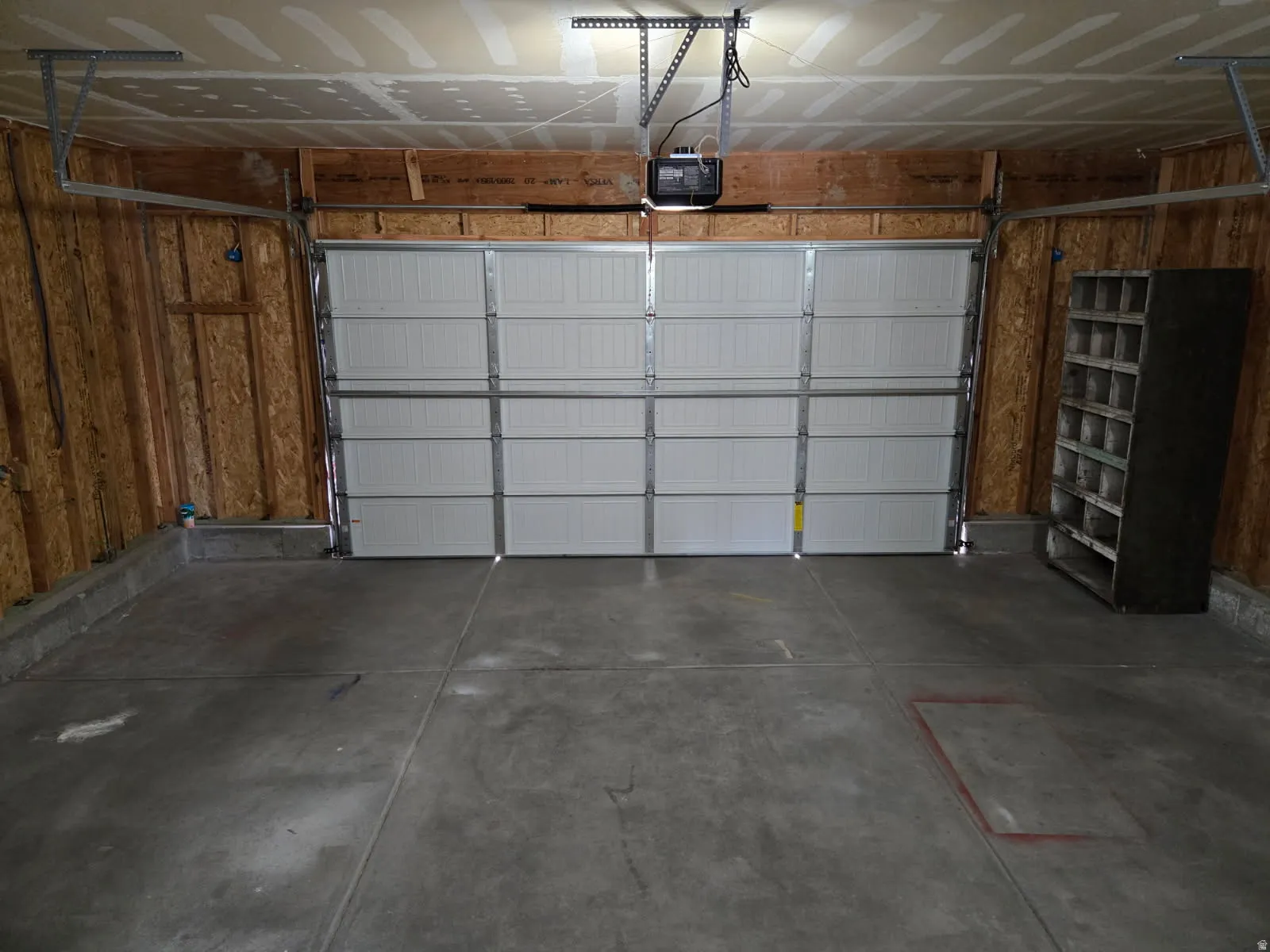 Garage space featuring a paneled overhead door, concrete flooring, exposed wood stud walls, and an overhead garage door opener system