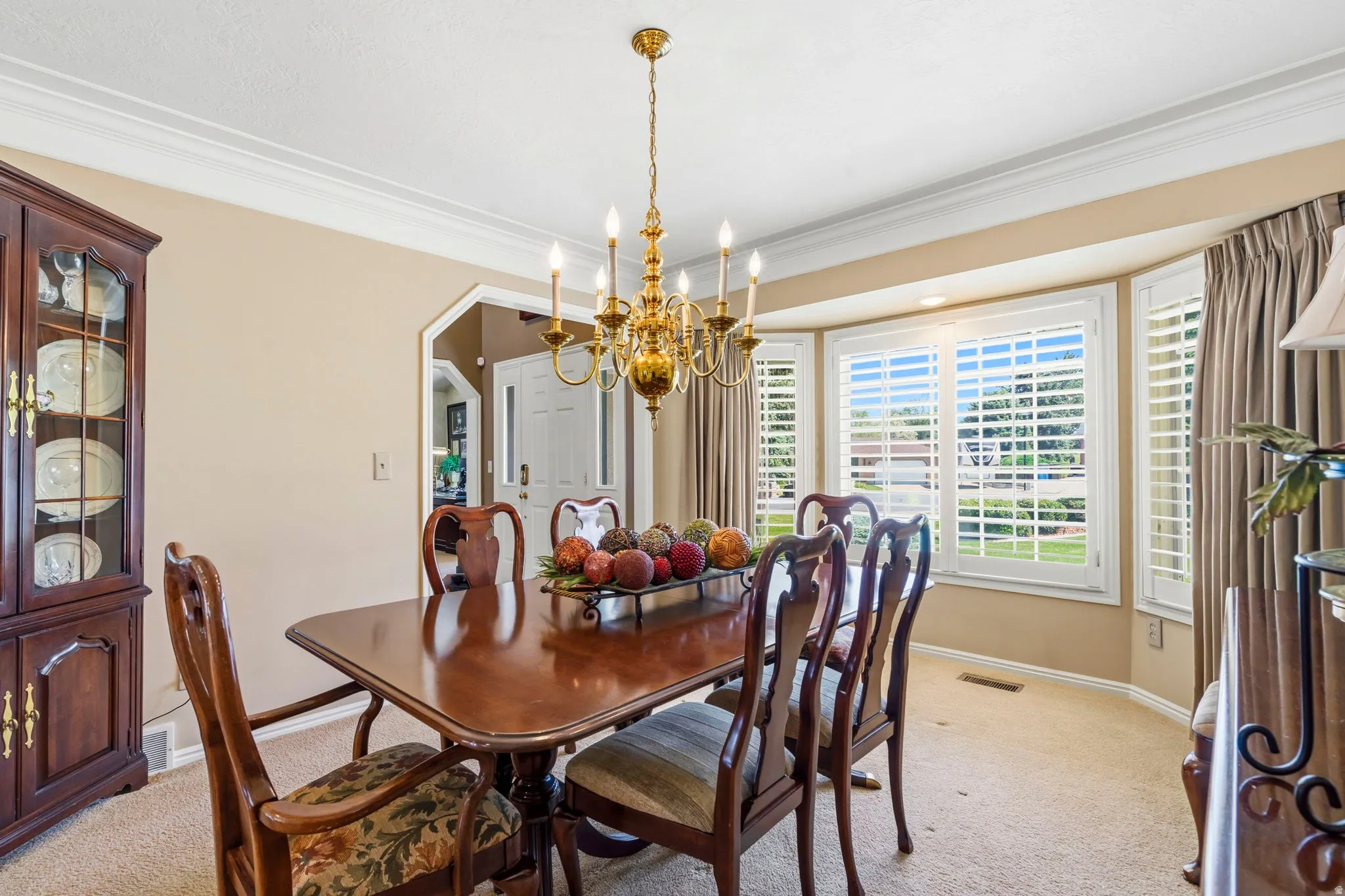 Dining area featuring a prominent bay window with plantation shutters, crown molding, and a brass chandelier
