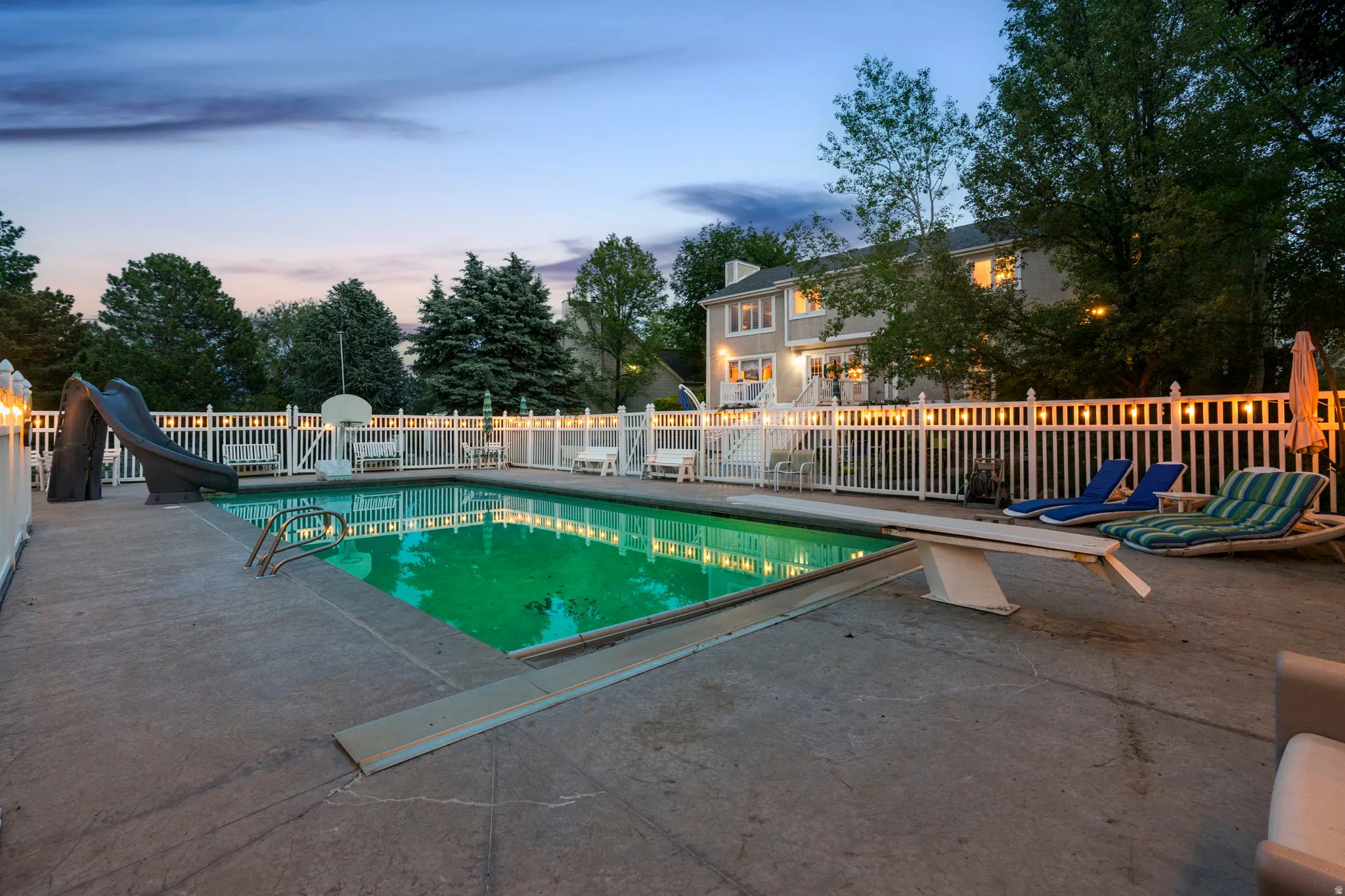 In-ground swimming pool with a diving board and a slide, surrounded by a concrete patio