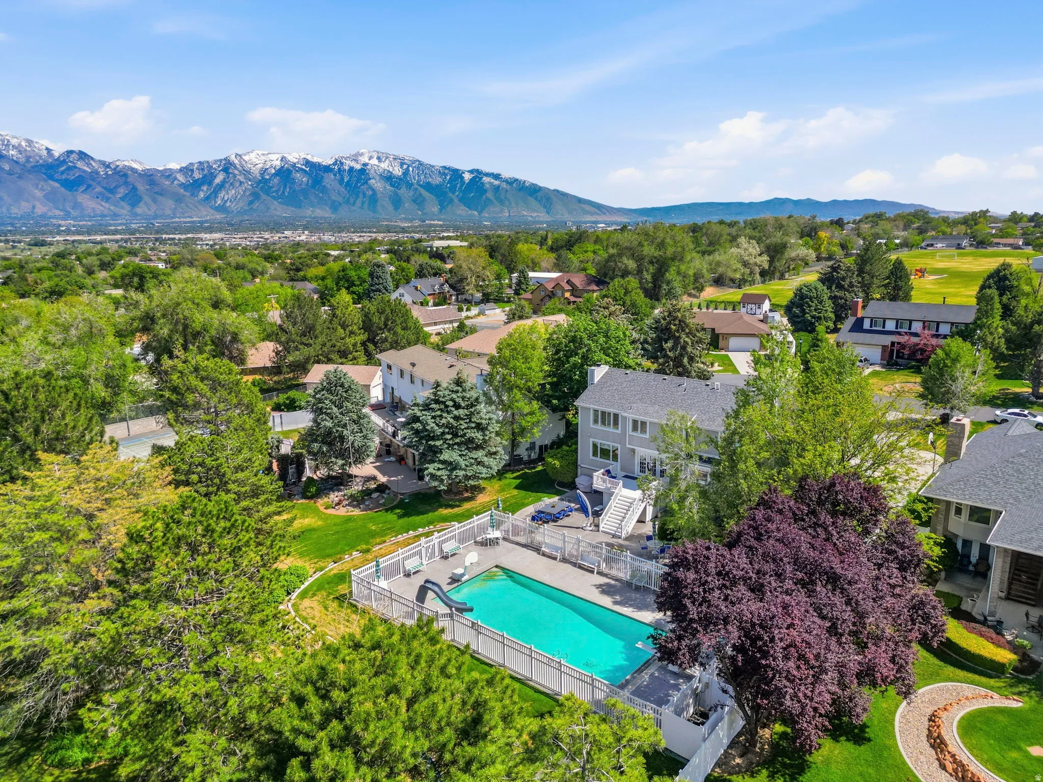 Rear exterior featuring a fenced swimming pool, spacious patio, and established landscaping