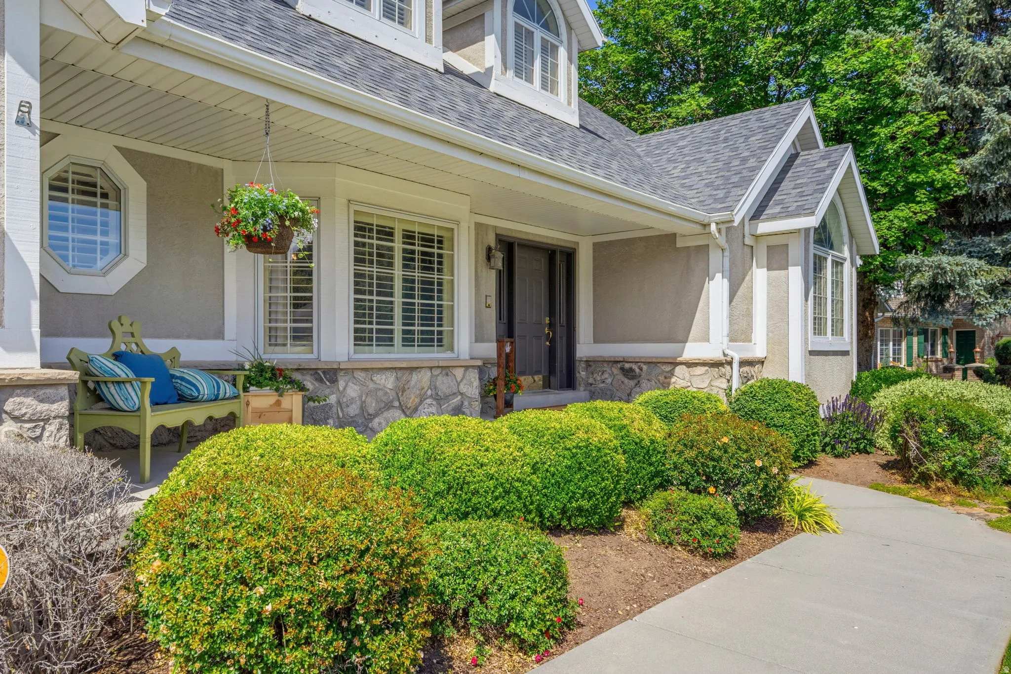 Front exterior featuring a covered porch, stone veneer skirting, multiple window styles, and a concrete pathway