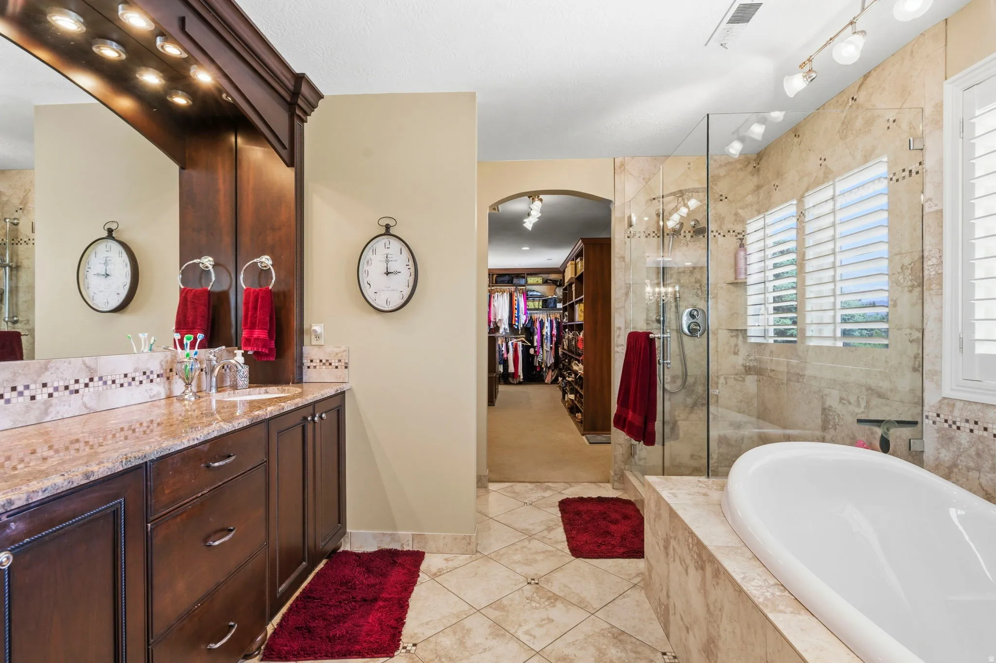 Bathroom featuring a built-in dark wood vanity with a light-colored countertop, an oversized mirror with integrated lighting, a freestanding soaking tub, and a glass-enclosed shower with tiled walls