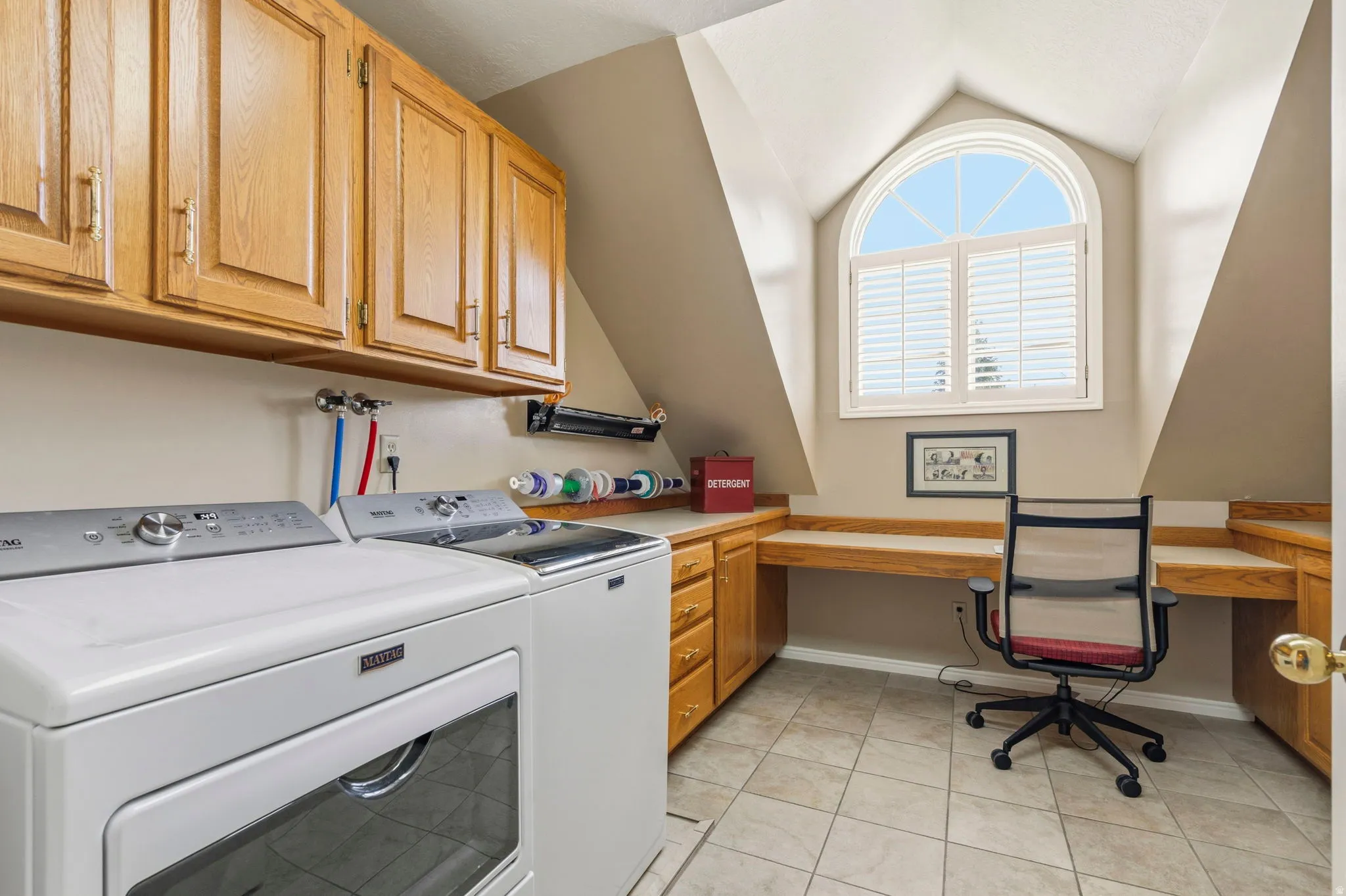 Dedicated utility area featuring a tiled floor, built-in cabinetry, and a large arched window with plantation shutters