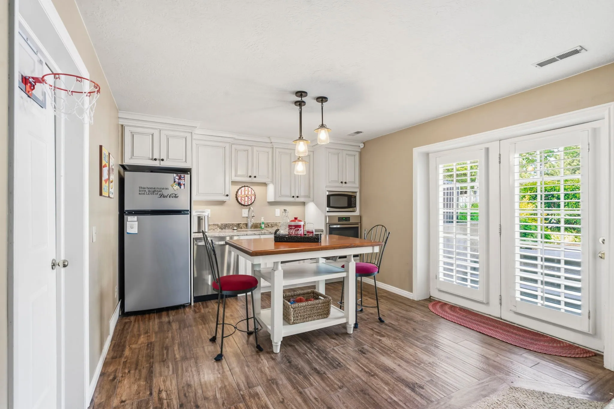 Kitchen area featuring white cabinetry, stainless steel appliances, wood-finish flooring, and pendant lighting