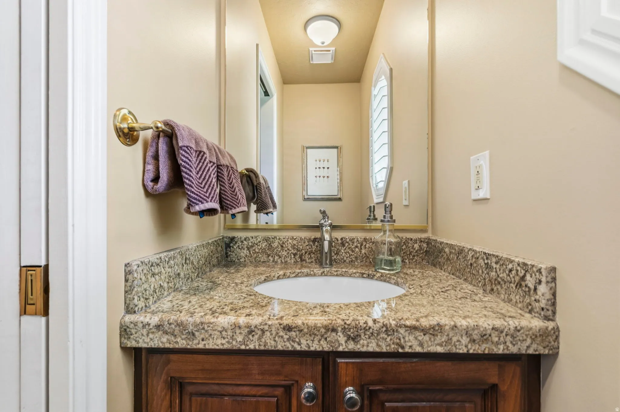 Bathroom vanity featuring a polished granite countertop with an integrated sink, a dark wood-finish cabinet, and a wall-mounted mirror