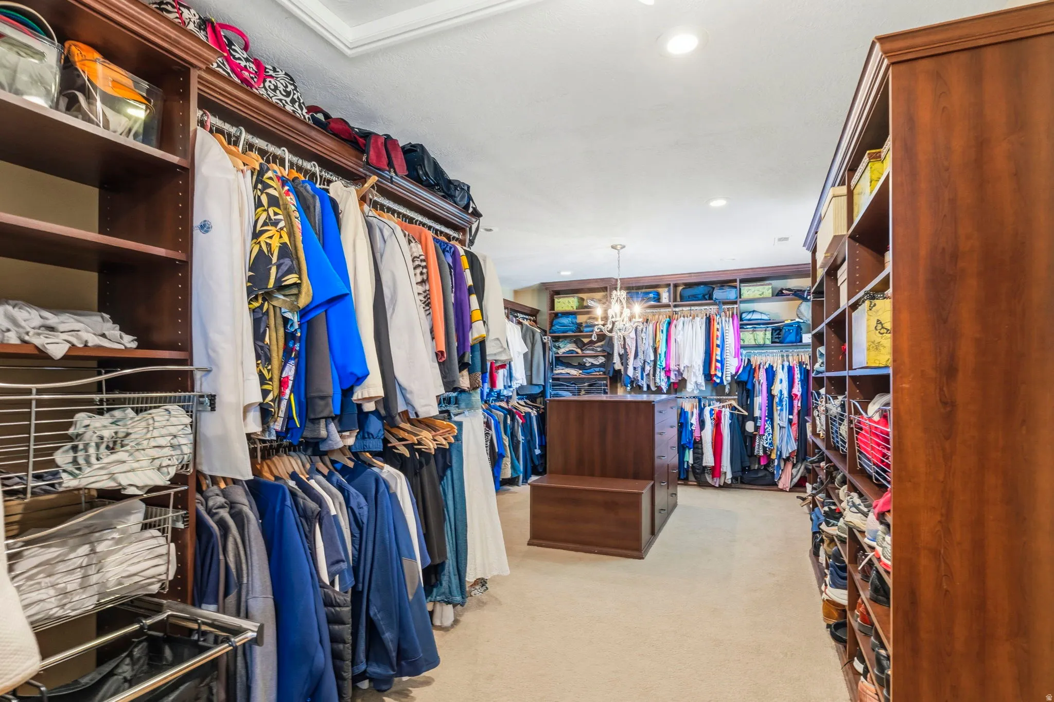 Spacious walk-in closet featuring extensive built-in cabinetry, varied shelving, garment rods, recessed lighting, and a central island with integrated storage