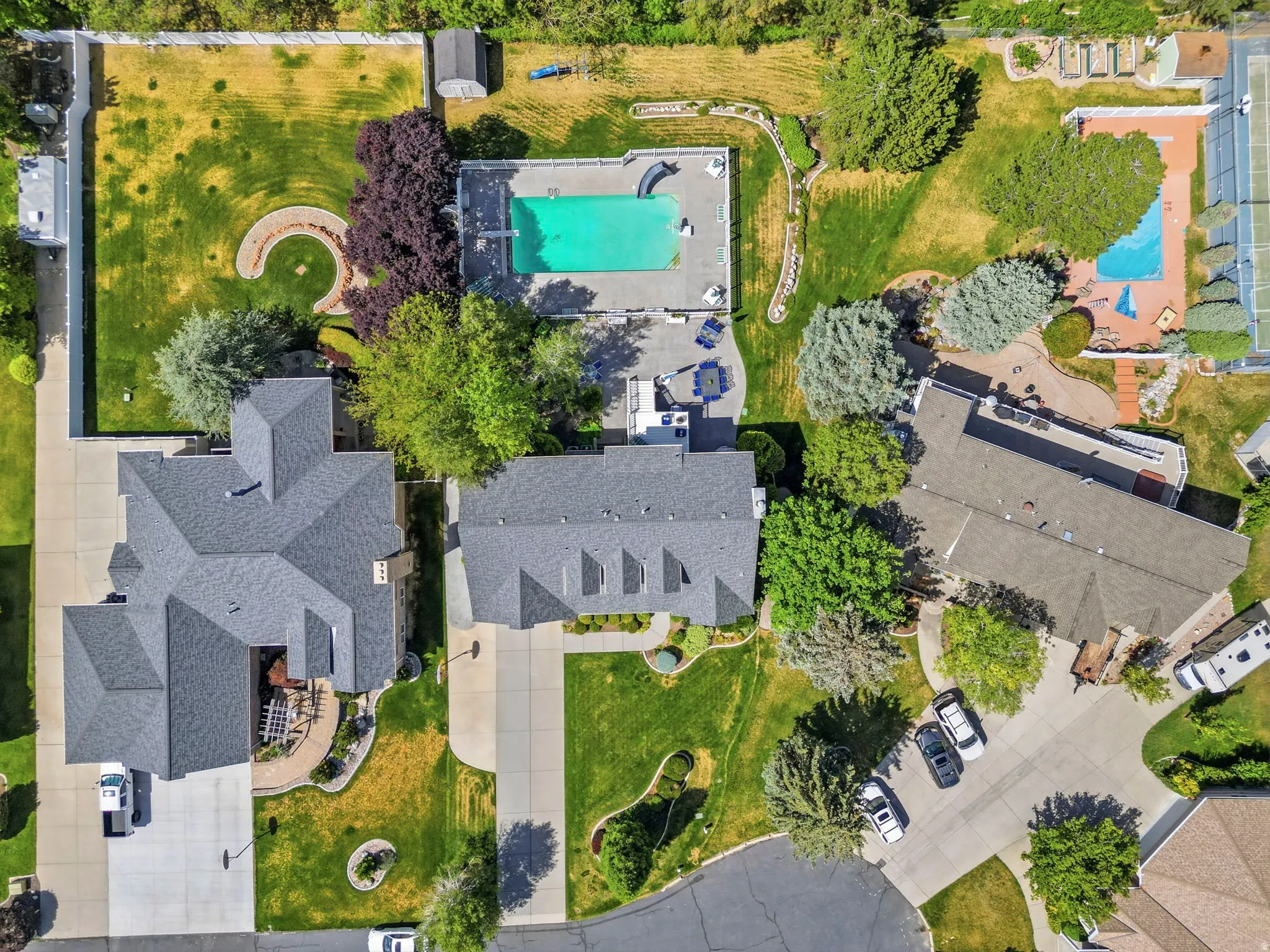 Expansive property featuring two distinct swimming pools, mature landscaping with various tree species, multiple paved driveways, and a tennis court
