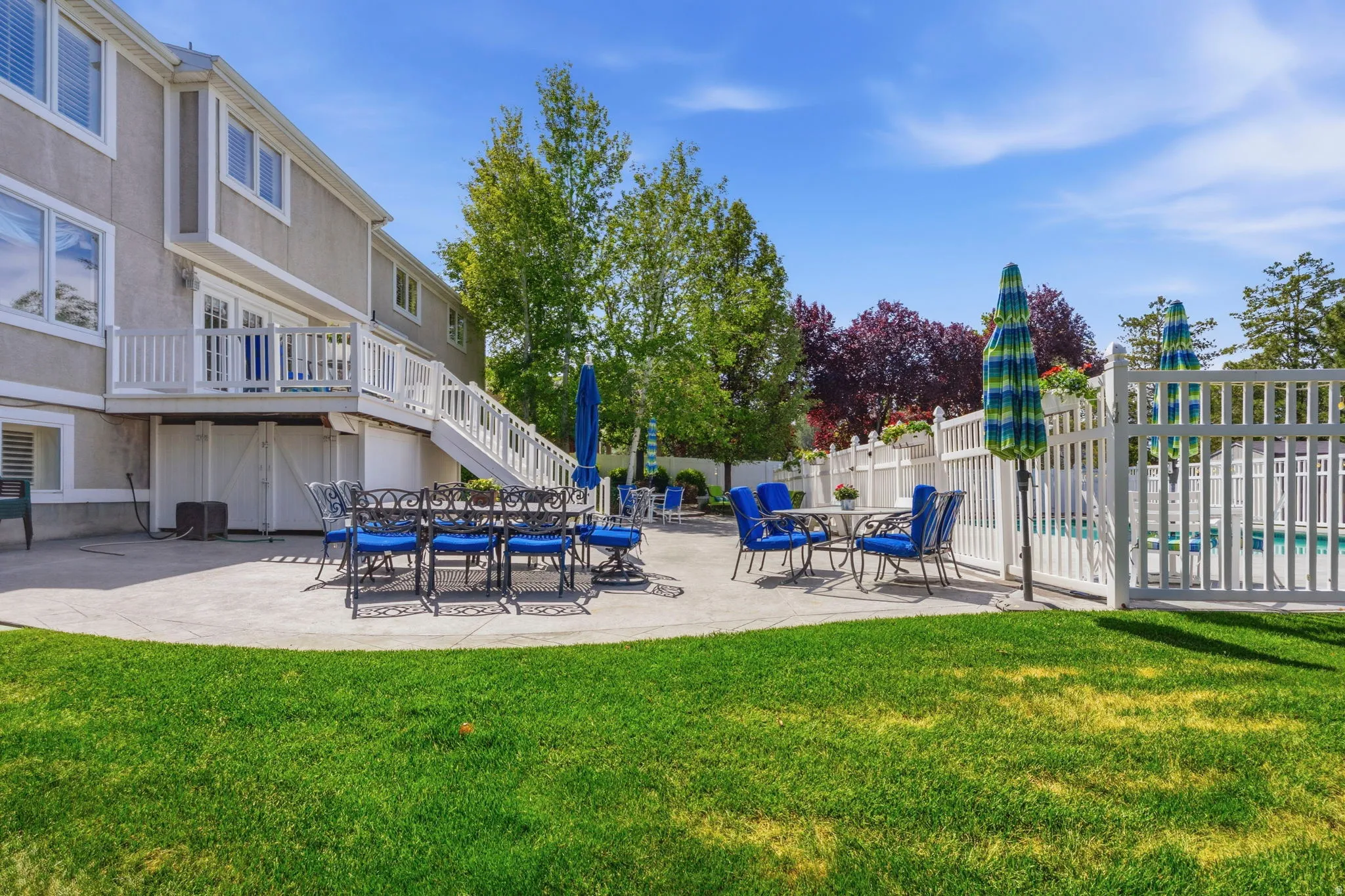 Expansive concrete patio with direct access from the upper deck, featuring a fenced-in pool area, green lawn, and mature landscaping