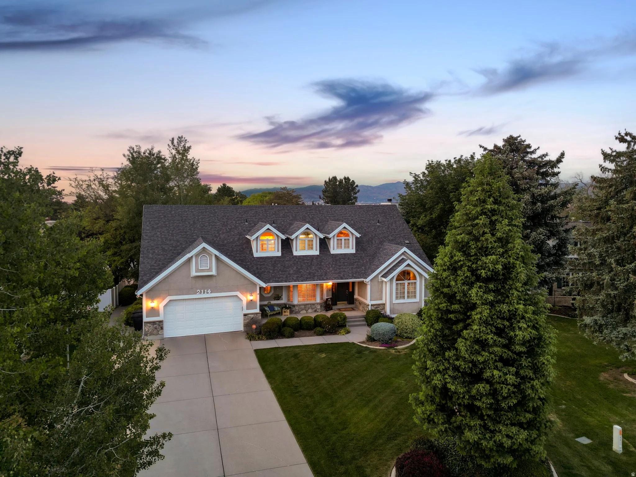 Traditional-style residence featuring a dormered roofline, stone veneer accents, and a two-car garage