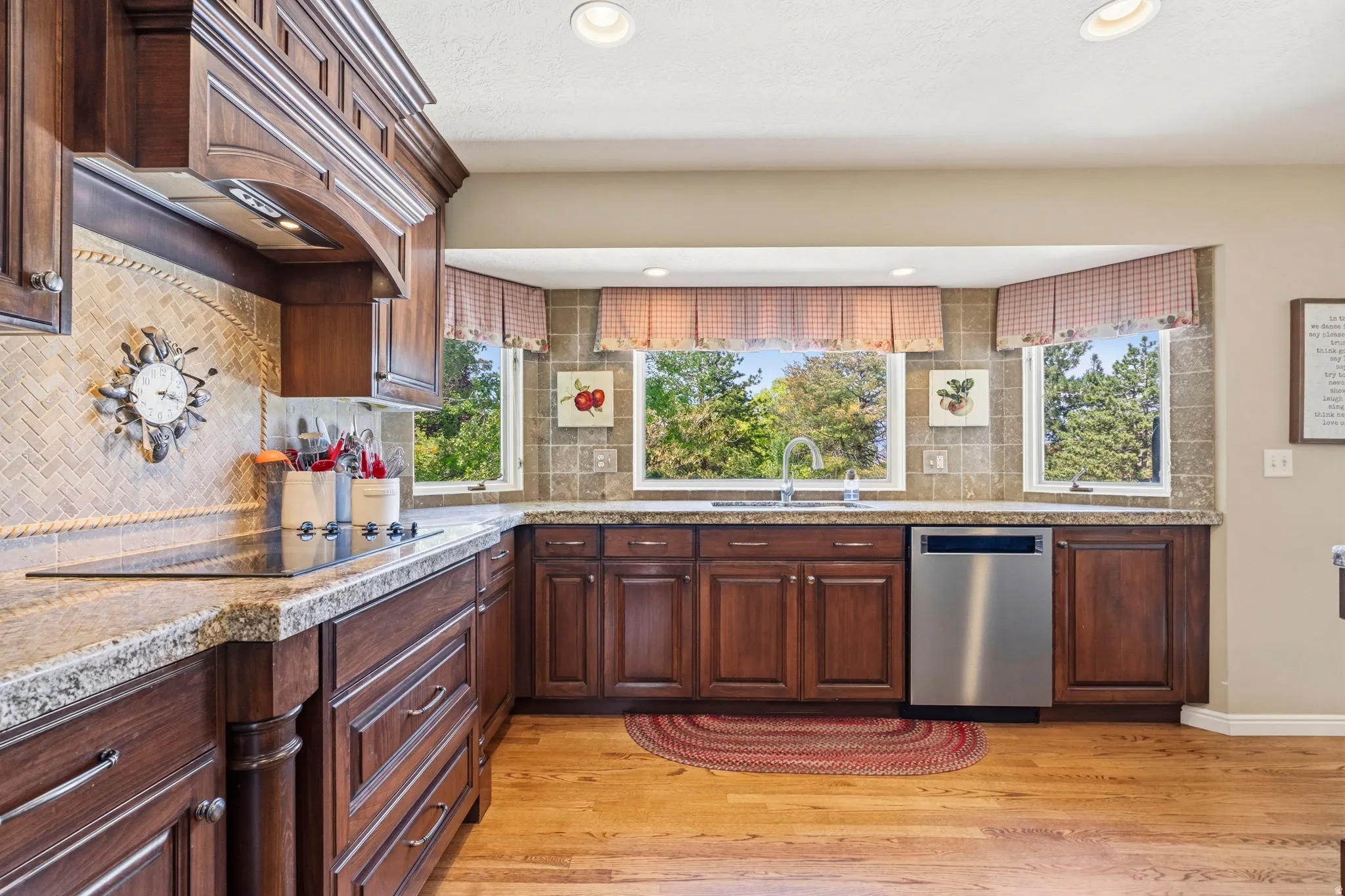 Kitchen featuring wood cabinetry, granite countertops, hardwood flooring, bay window, and stainless steel dishwasher