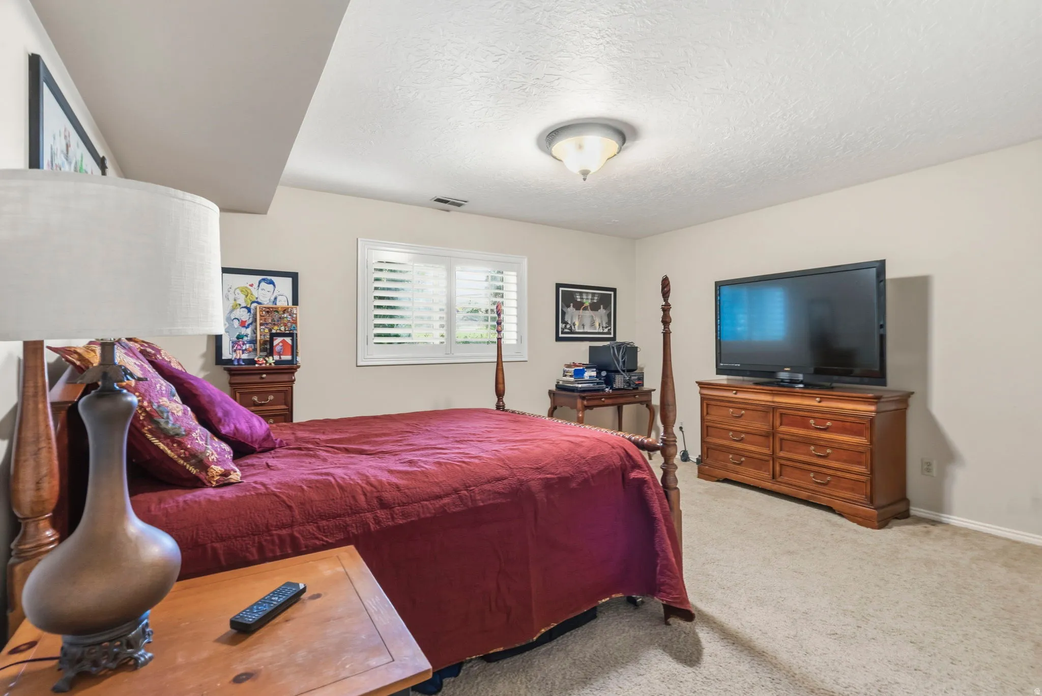 Spacious bedroom featuring neutral wall tones, textured carpet flooring, and a ceiling-mounted light fixture