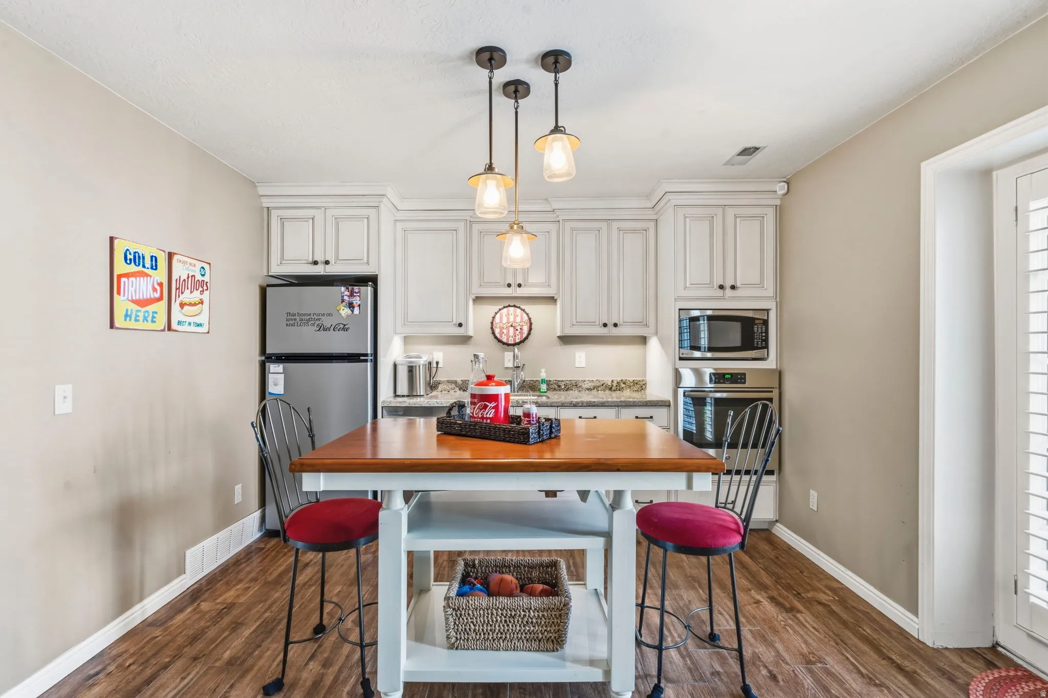Kitchenette featuring an integrated stainless steel microwave and oven, a built-in stainless steel refrigerator, white cabinetry, a wood-finish island with shelving, and wood-finish flooring