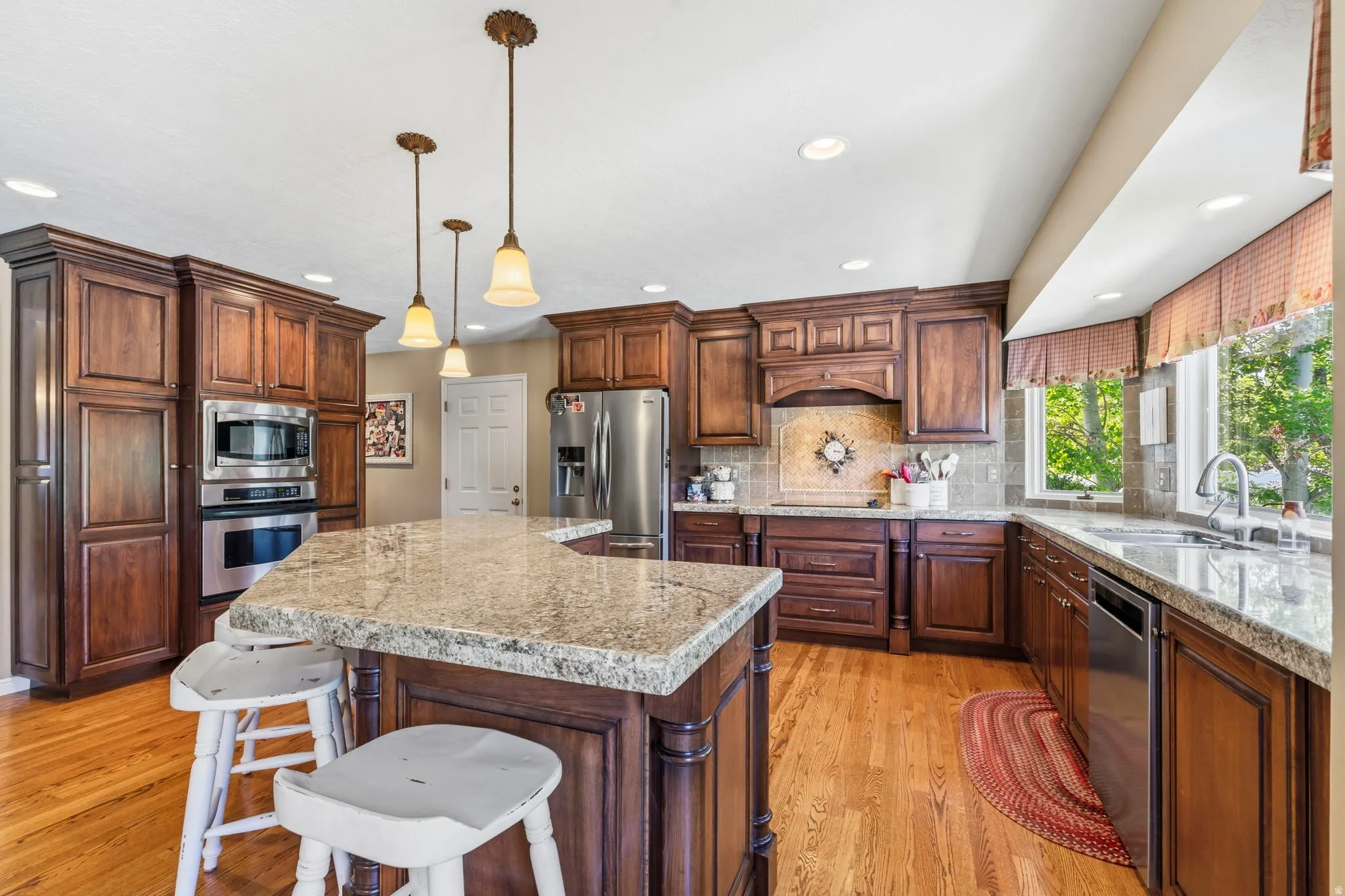 Open-concept kitchen featuring wood-finish flooring, custom wood cabinetry, a large kitchen island with a stone countertop, stainless steel appliances, and recessed lighting