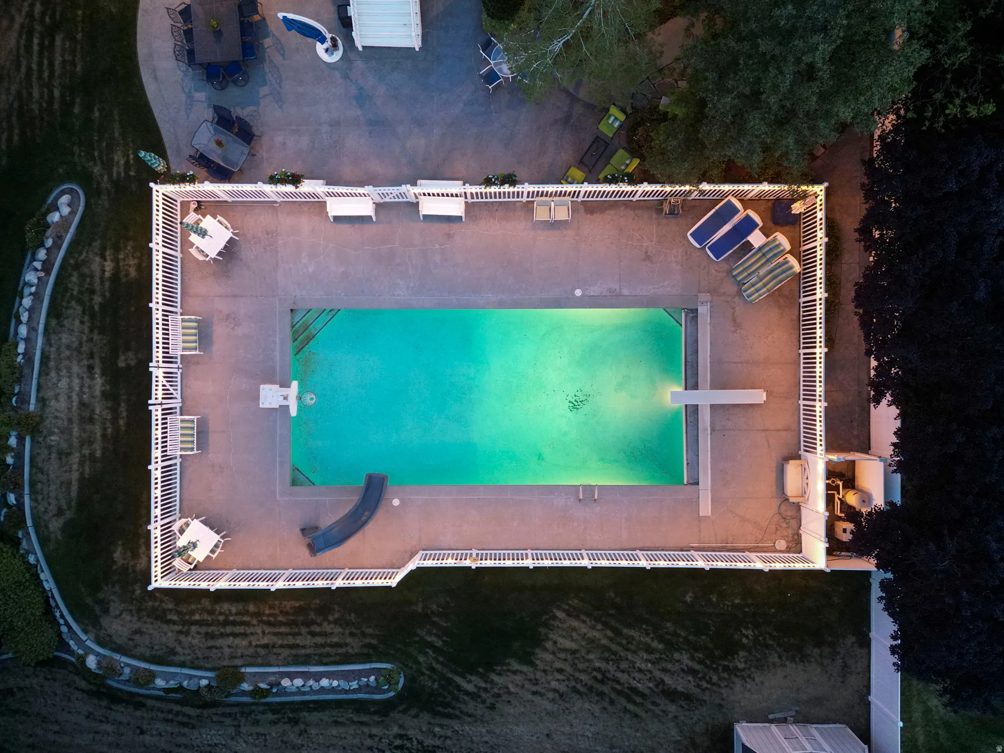 In-ground swimming pool featuring a diving board, concrete surround, white picket fence, and integrated slide
