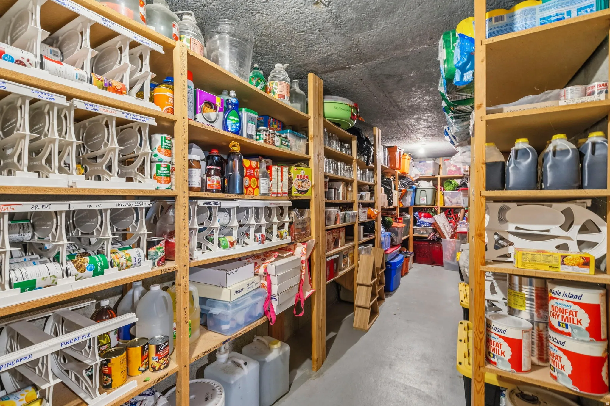 Dedicated storage room featuring extensive built-in wooden shelving units, grey concrete flooring, and overhead lighting