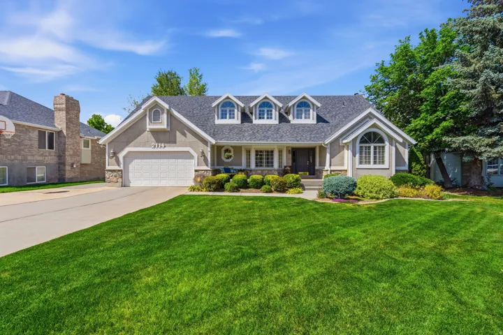 Stucco and stone facade home featuring a two-car garage, dormer windows, and a manicured lawn