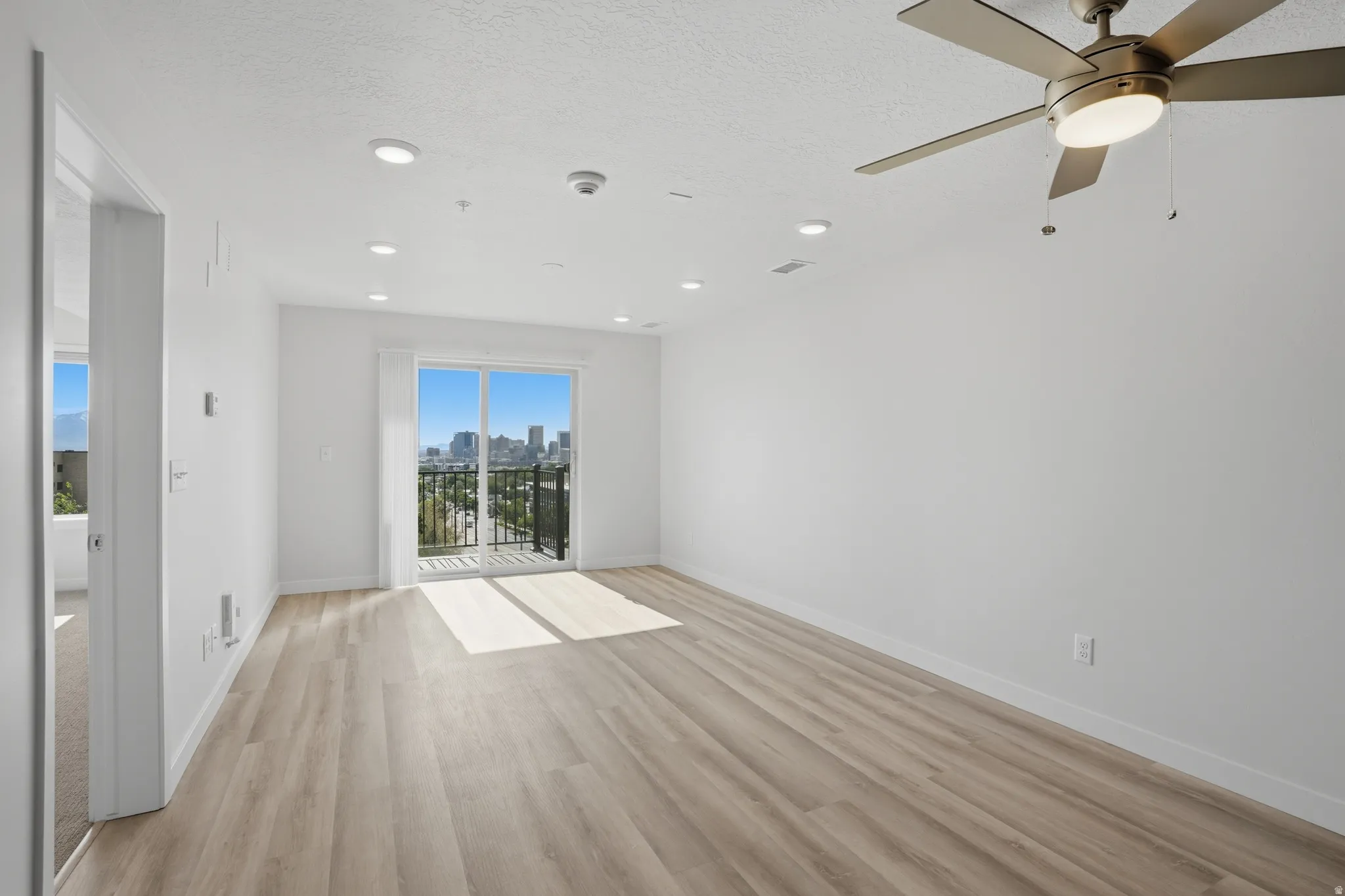 Spacious living room with luxury flooring, recessed lighting, and sliding glass doors leading to a private balcony with spectacular views of the city