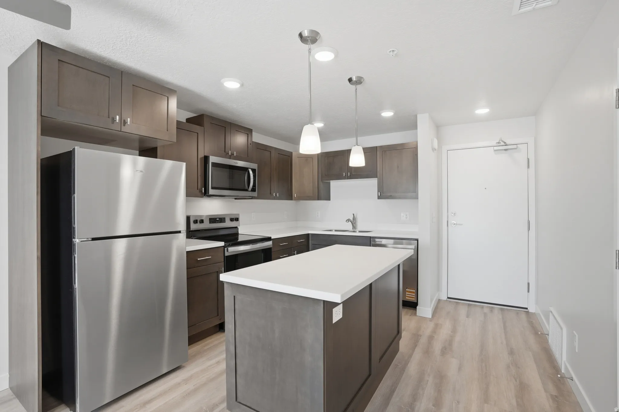 Open-concept kitchen and living area featuring a central island with white quartz countertops, beautiful cabinetry, and stainless steel appliances