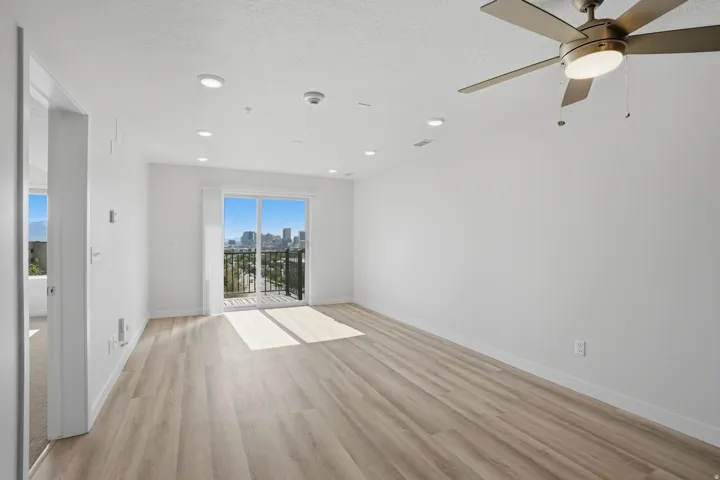 Spacious living room with luxury flooring, recessed lighting, and sliding glass doors leading to a private balcony with spectacular views of the city