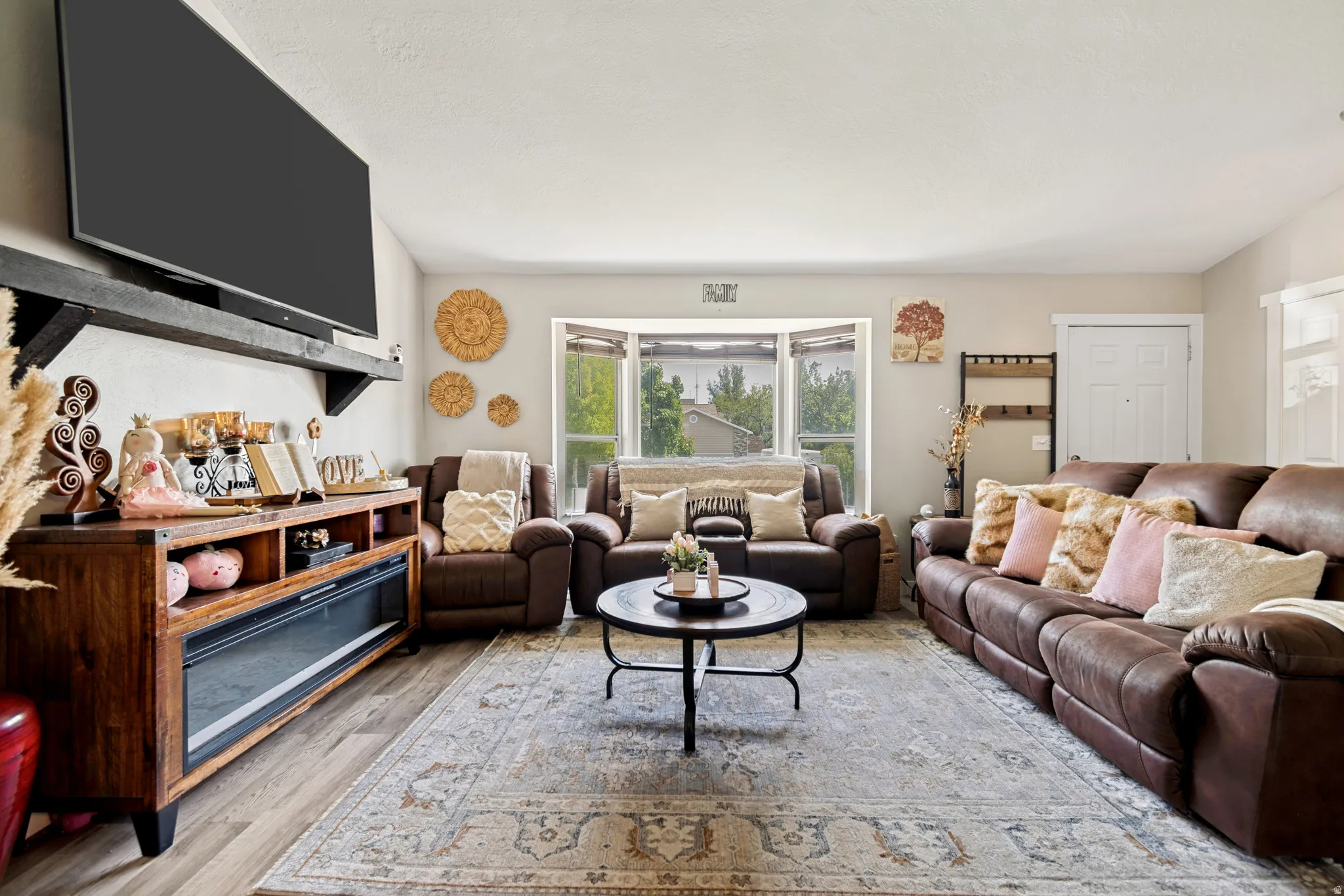 Living area featuring wood-finish flooring, a decorative area rug, and a bay window with natural light