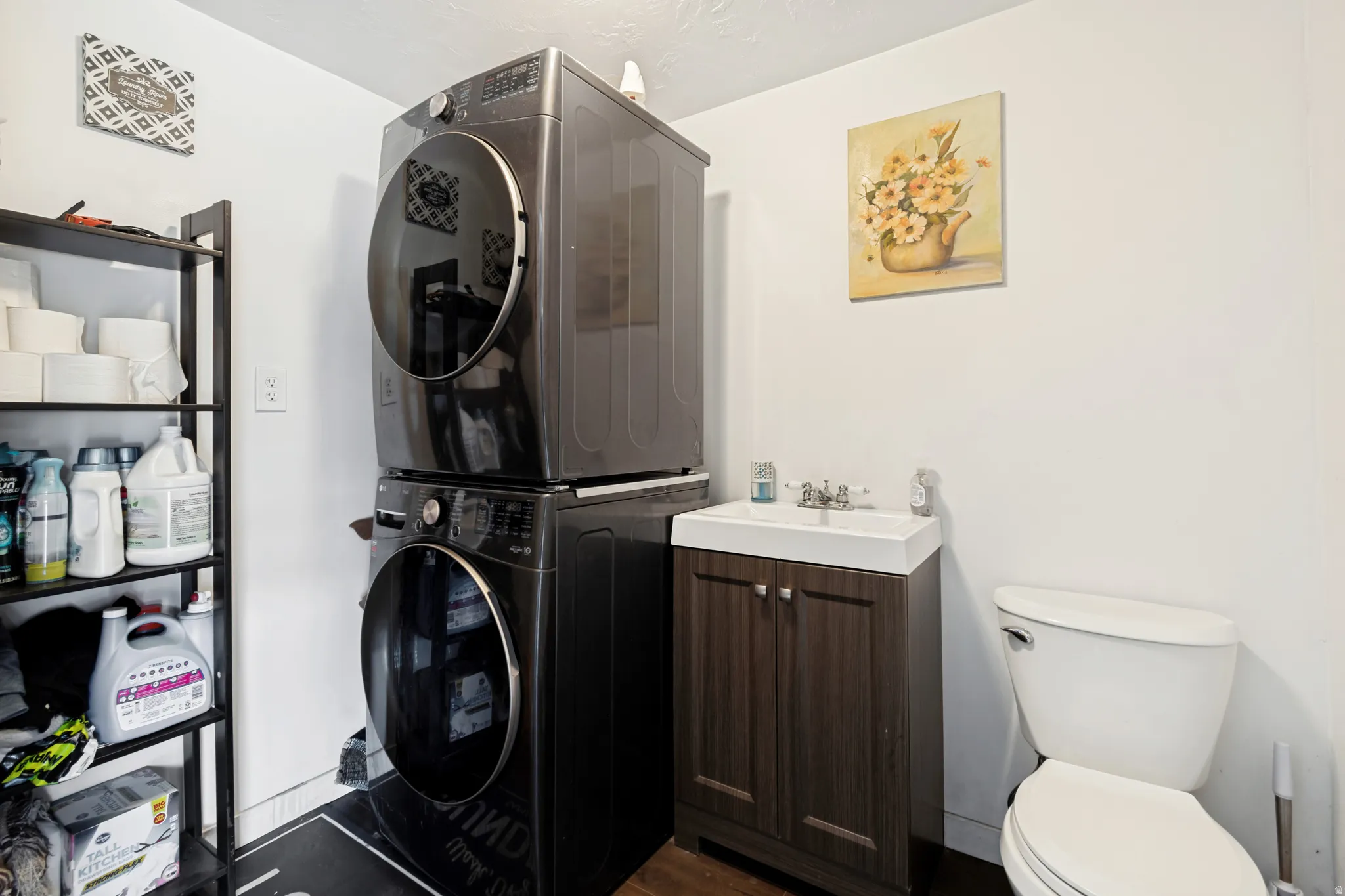 Dedicated laundry area featuring a stacked washer and dryer, a vanity with an integrated sink, a two-door base cabinet, and a toilet