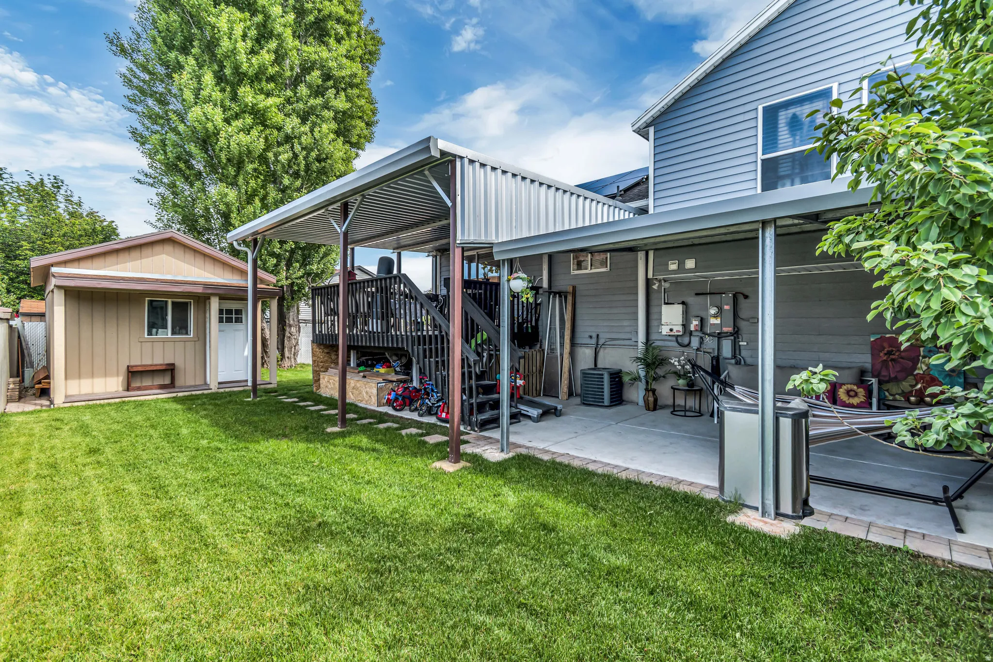 Expansive backyard featuring a manicured lawn, a detached storage shed, a covered patio area, and a raised wood-deck with stairs