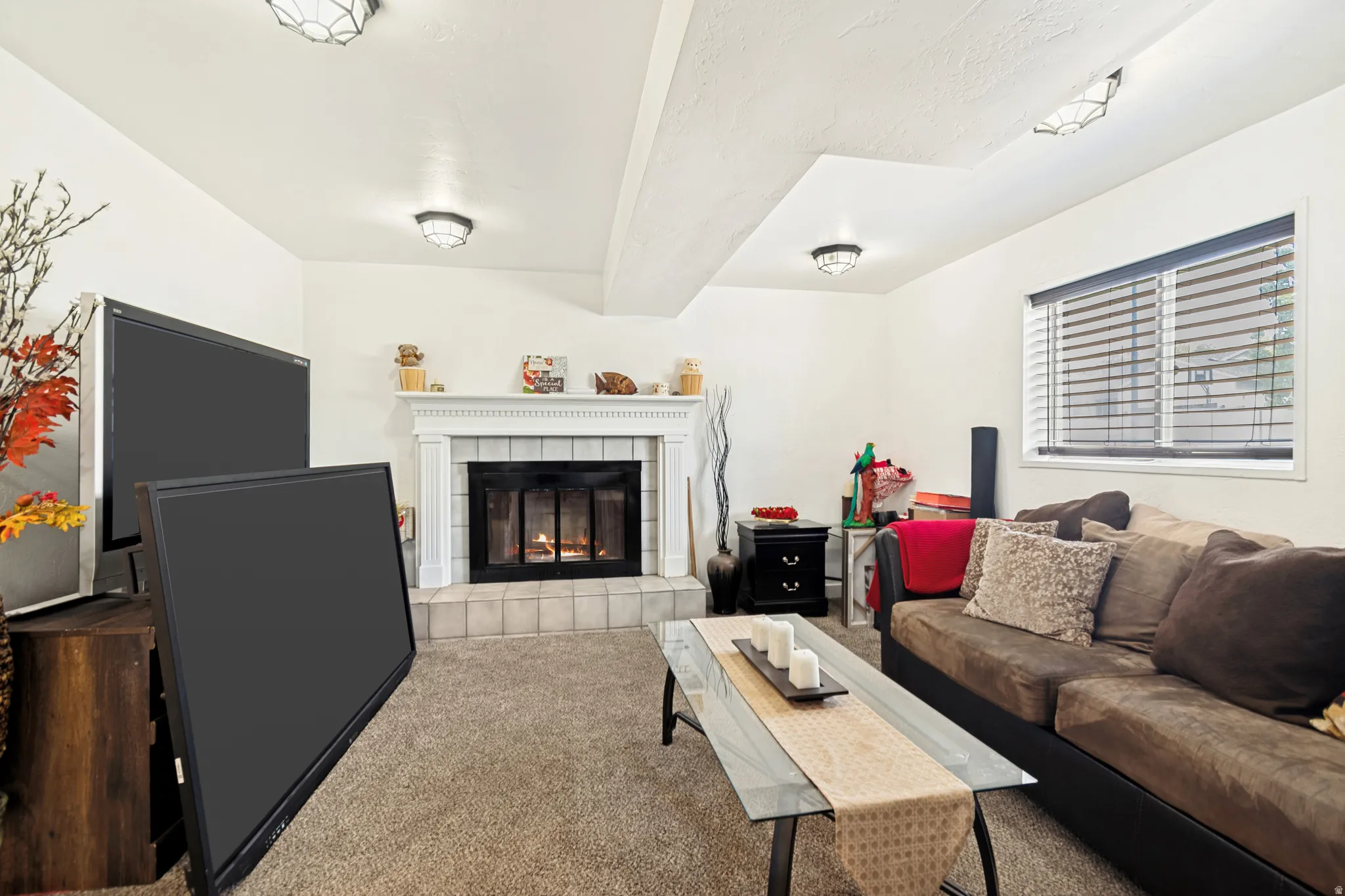Living area featuring a white mantel fireplace with tile surround, a window with blinds, and recessed lighting