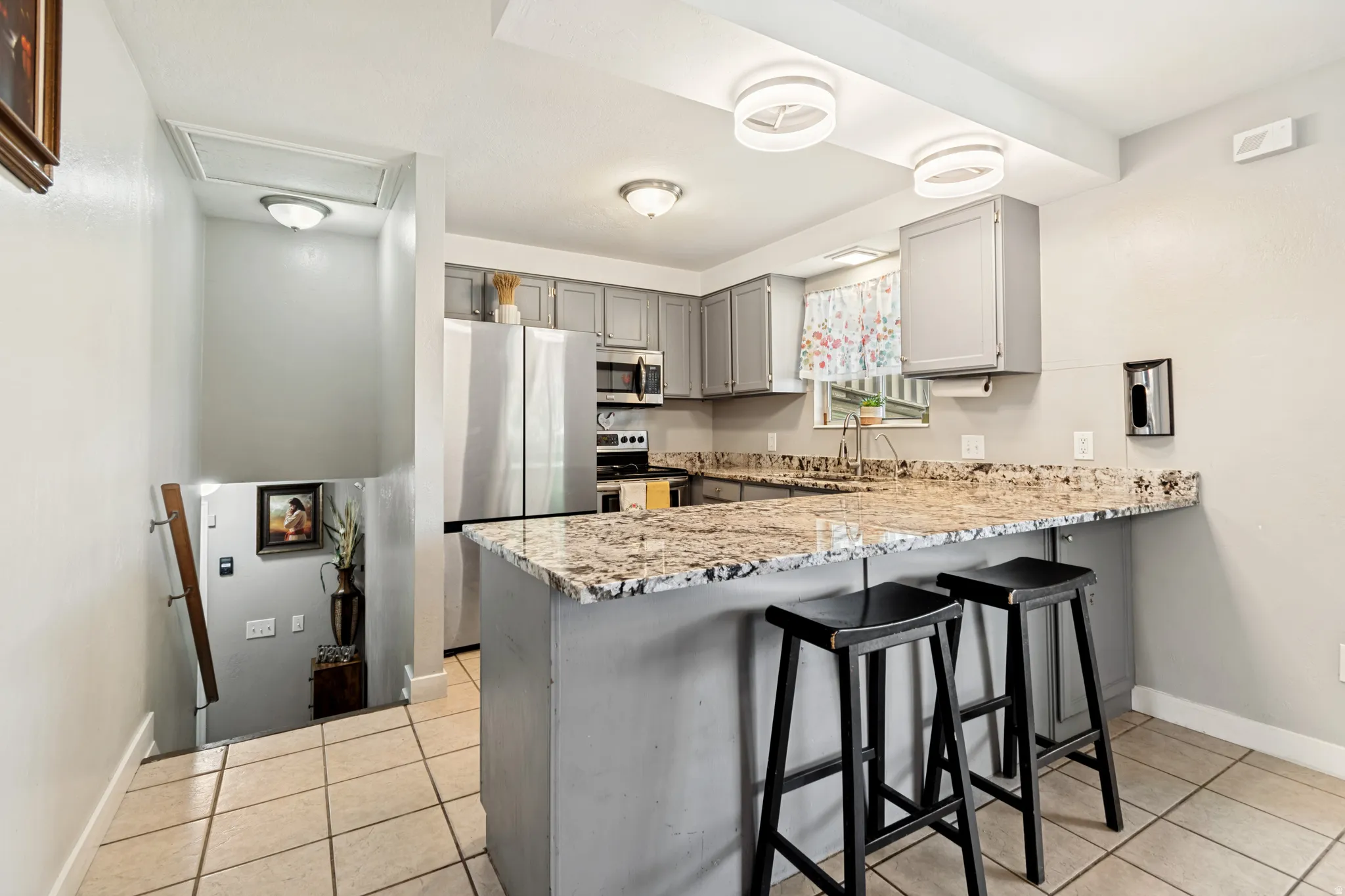 Kitchen featuring gray cabinetry, stainless steel appliances, speckled stone countertops, and a breakfast bar with seating