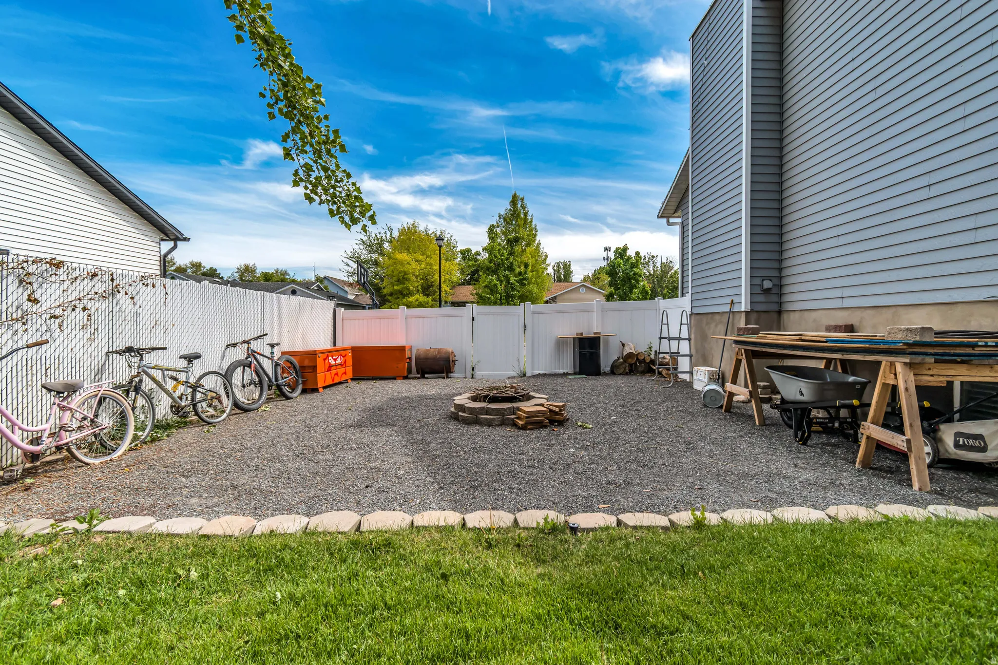 Gravel yard featuring a stone-lined fire pit, white vinyl privacy fencing, and a manicured lawn border
