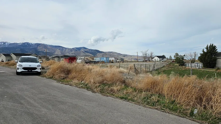 Expansive undeveloped lot featuring a paved road frontage, established fencing, and visible mountain scenery