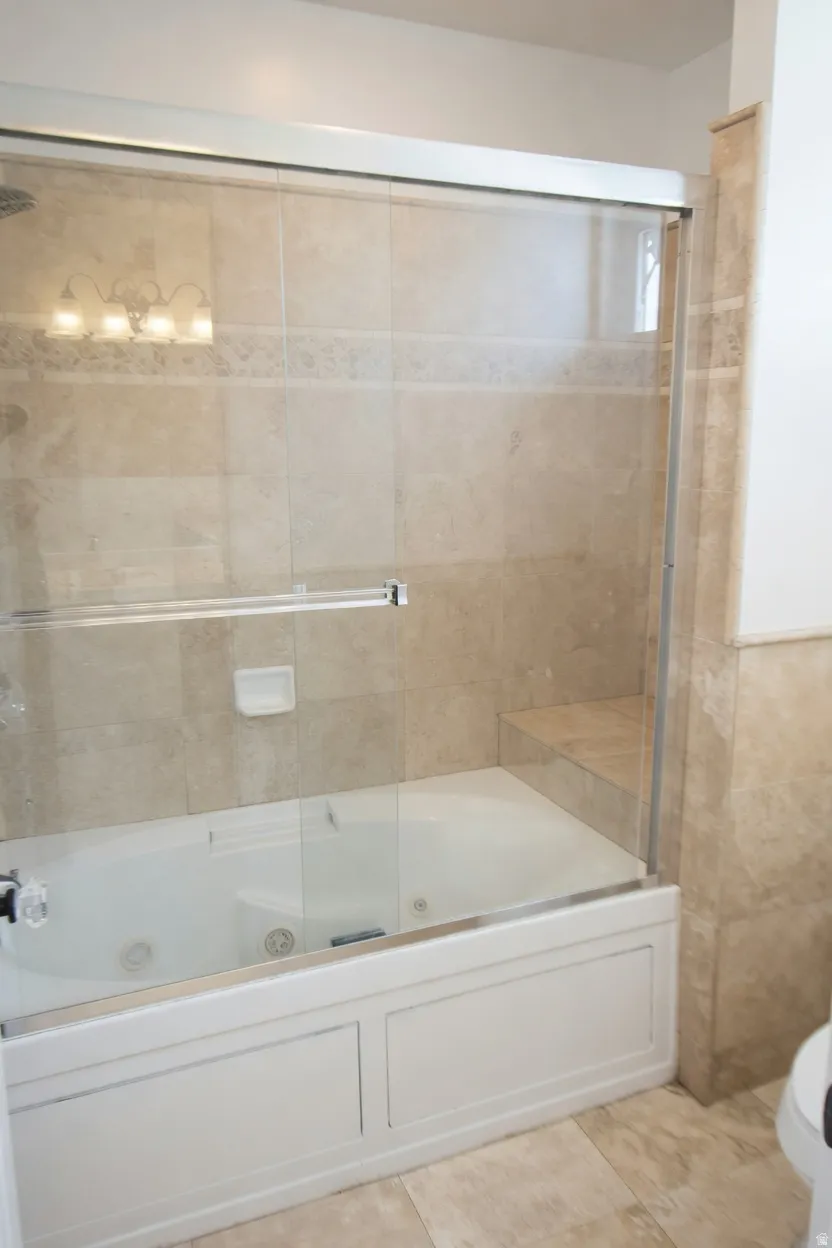Tub and shower combination with sliding glass doors, surrounded by large format tile with a decorative accent band, and featuring a built-in shower bench, toilet.