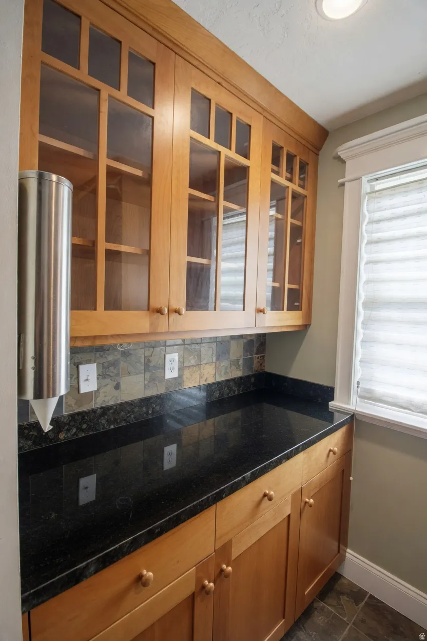 Crafted wood cabinetry with clear glass door fronts, dark stone countertops, natural stone backsplash, and recessed lighting