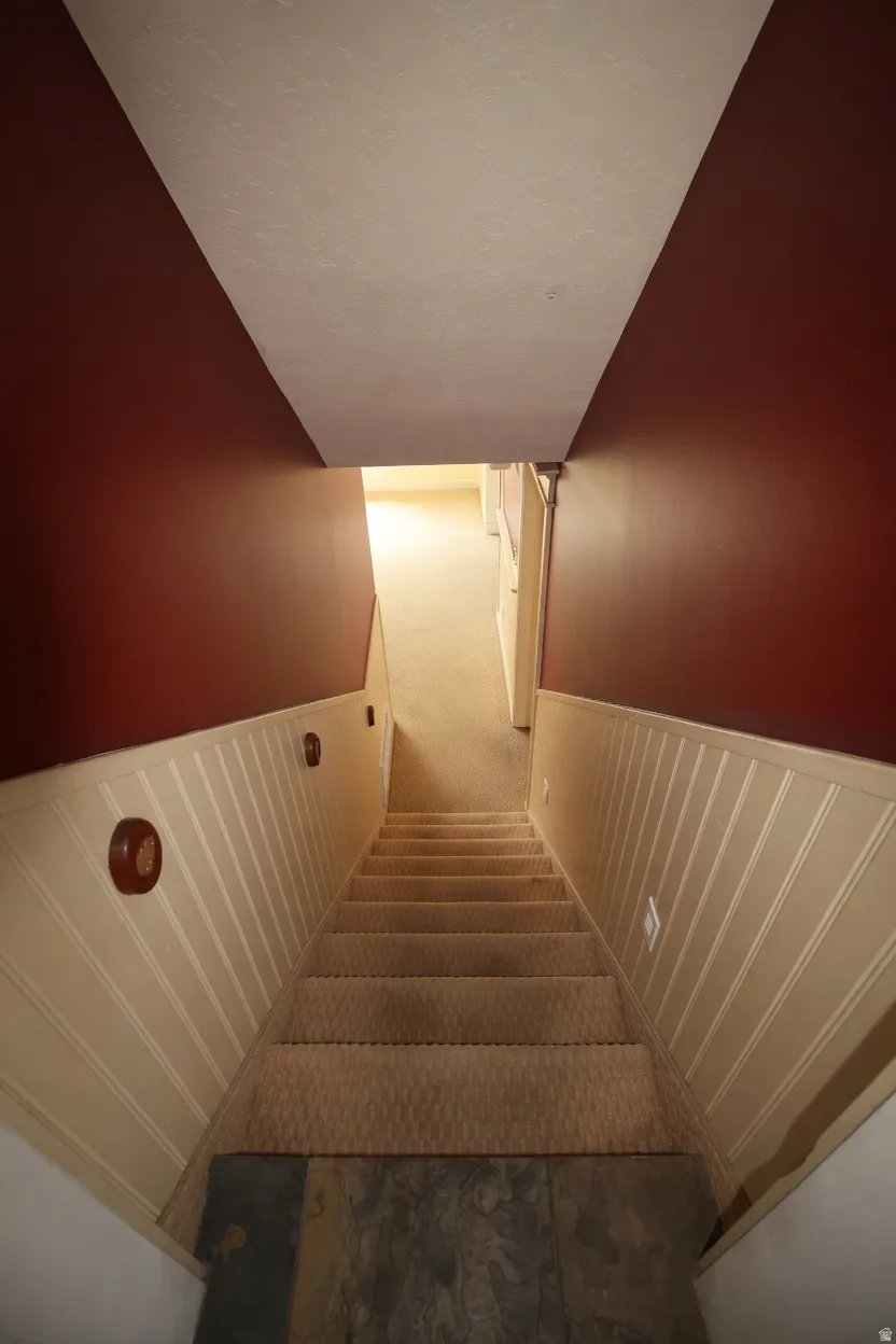 Carpeted staircase featuring beadboard wainscoting and wall sconces, descending to a slate tile landing