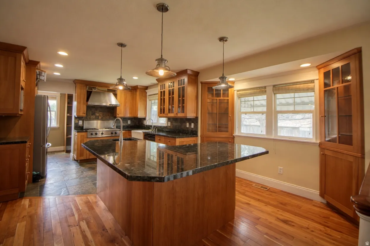Expansive kitchen featuring a large central island with a stone countertop, custom wood cabinetry, stainless steel appliances, and recessed lighting