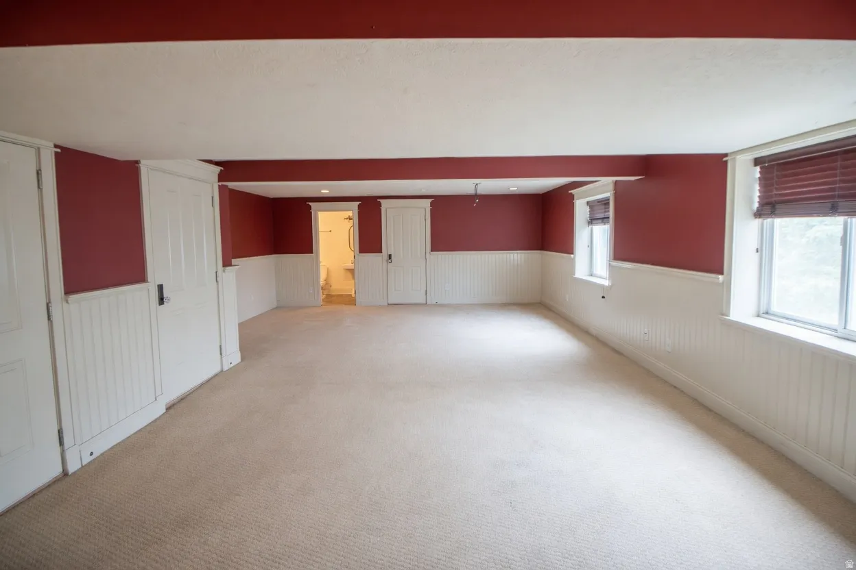 Spacious interior room featuring crimson walls over white wainscoting, light-toned carpet flooring, and multiple windows with included blinds