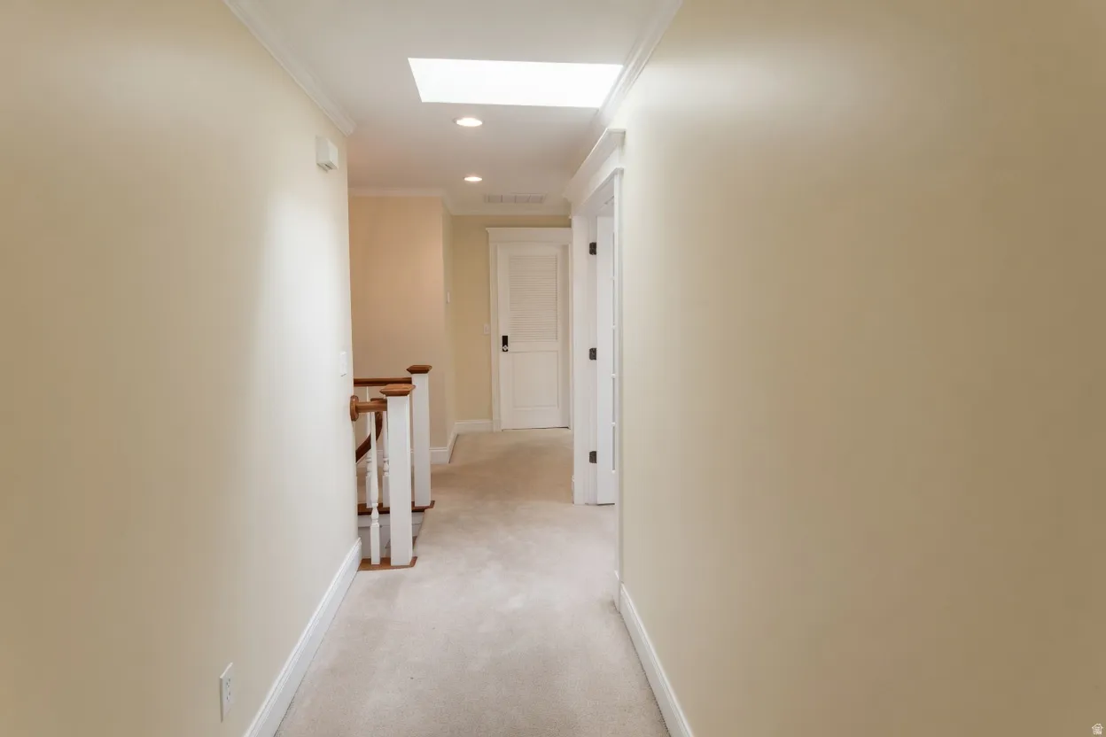 Carpeted hallway featuring a skylight, recessed lighting, crown molding, white trim, and a white baluster and wood-finish handrail