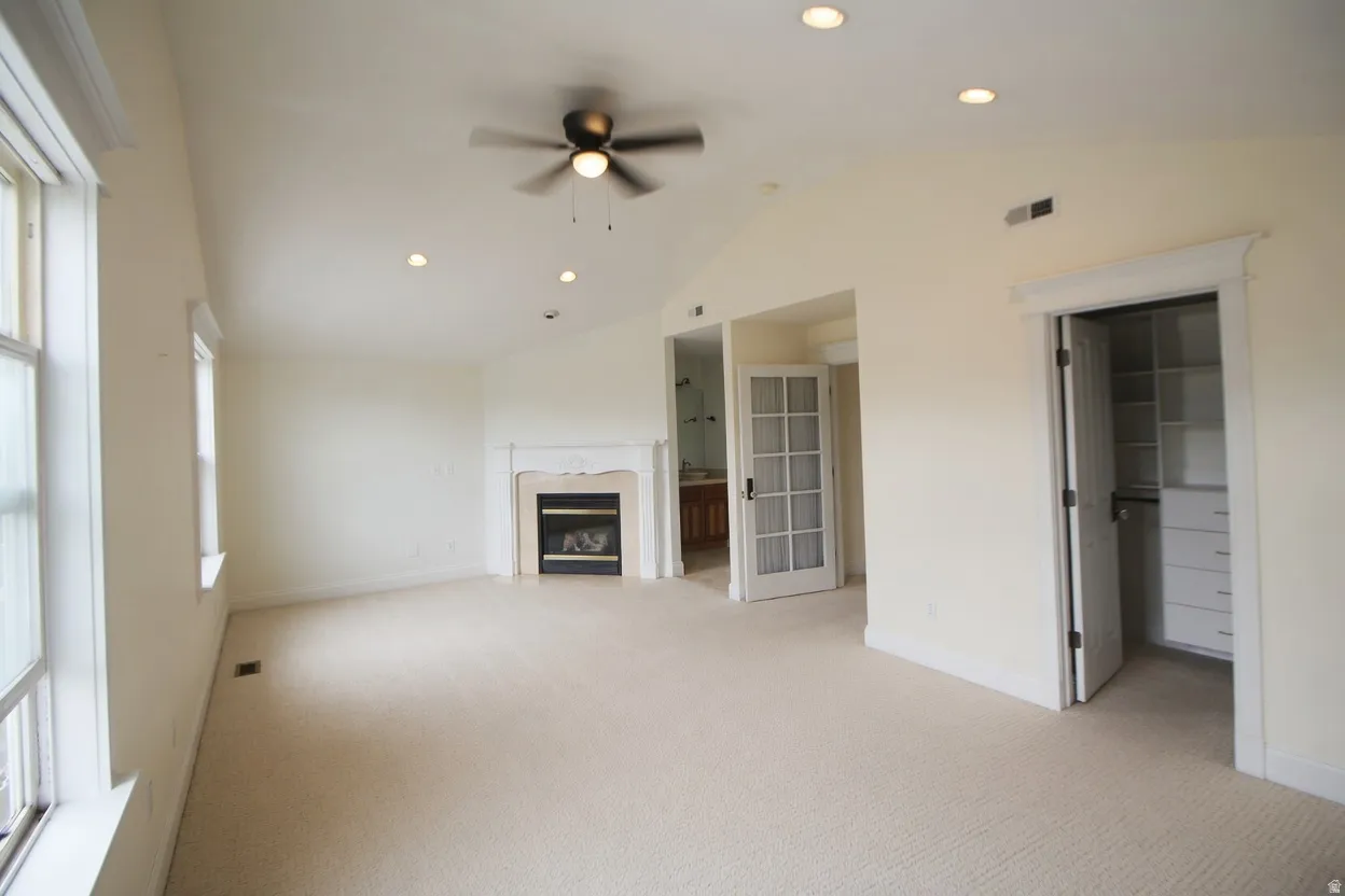 Spacious Master bedroom featuring vaulted ceilings, recessed lighting, a ceiling fan, a fireplace with a light-toned mantel, and multiple windows