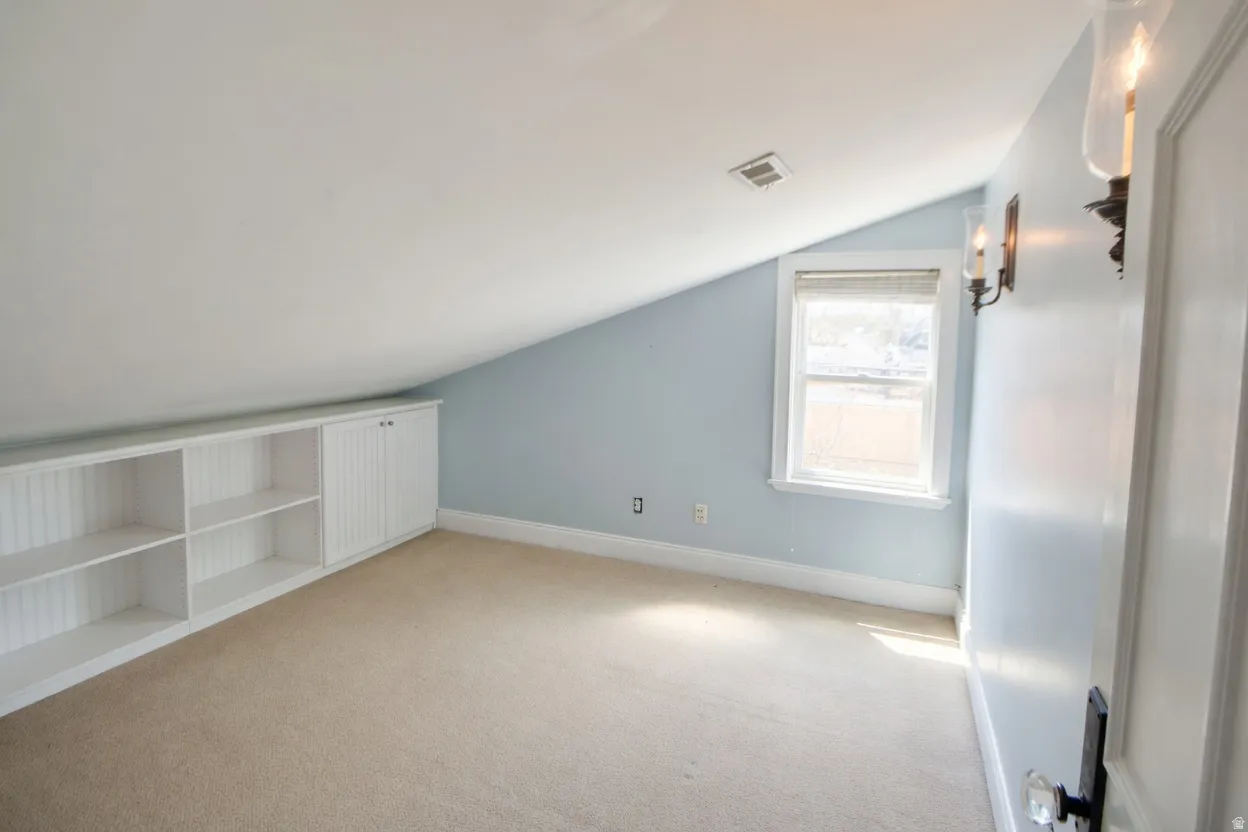 Bedroom 4 or nursery sloped ceiling room featuring a built-in white storage unit with shelving and cabinetry, a single window, and two wall sconces