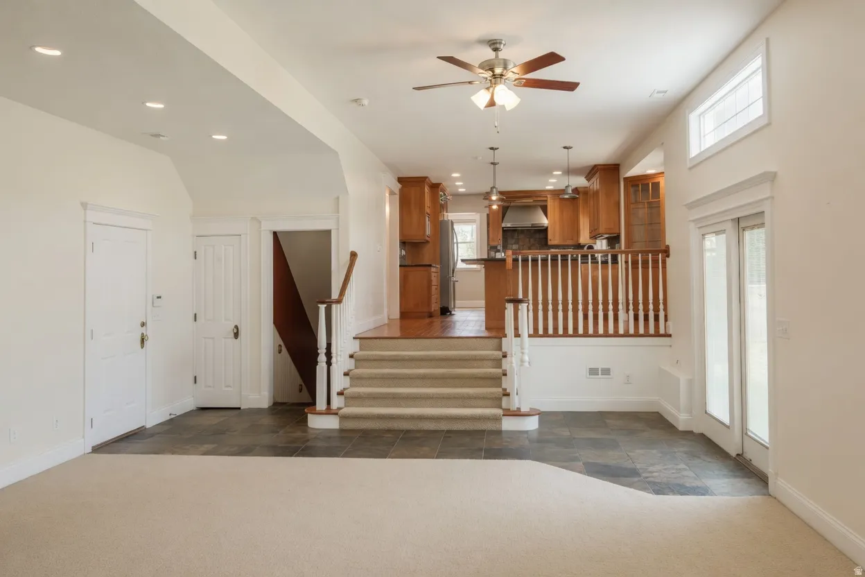 Multi-level interior featuring a kitchen with wood cabinetry and pendant lighting, a ceiling fan, recessed lighting, and a partial staircase with wood handrails