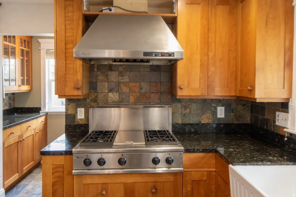 Professional-grade stainless steel range with overhead ventilation hood, complemented by rich wood cabinetry and dark, speckled countertops